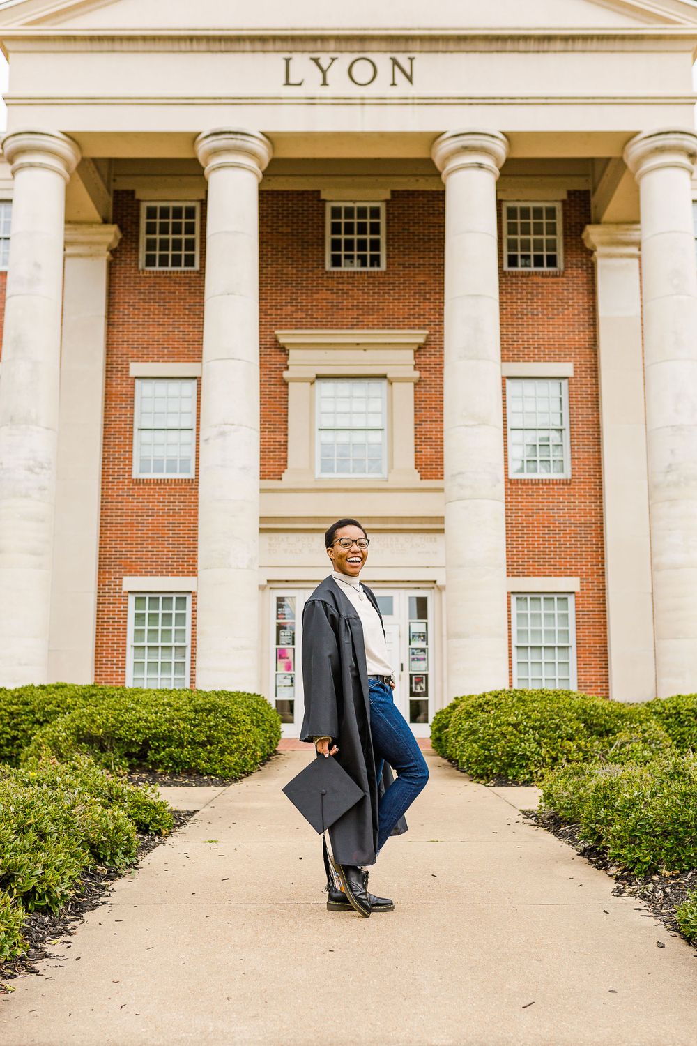 Graduate poses with diploma in front of historic Lyon building entrance.