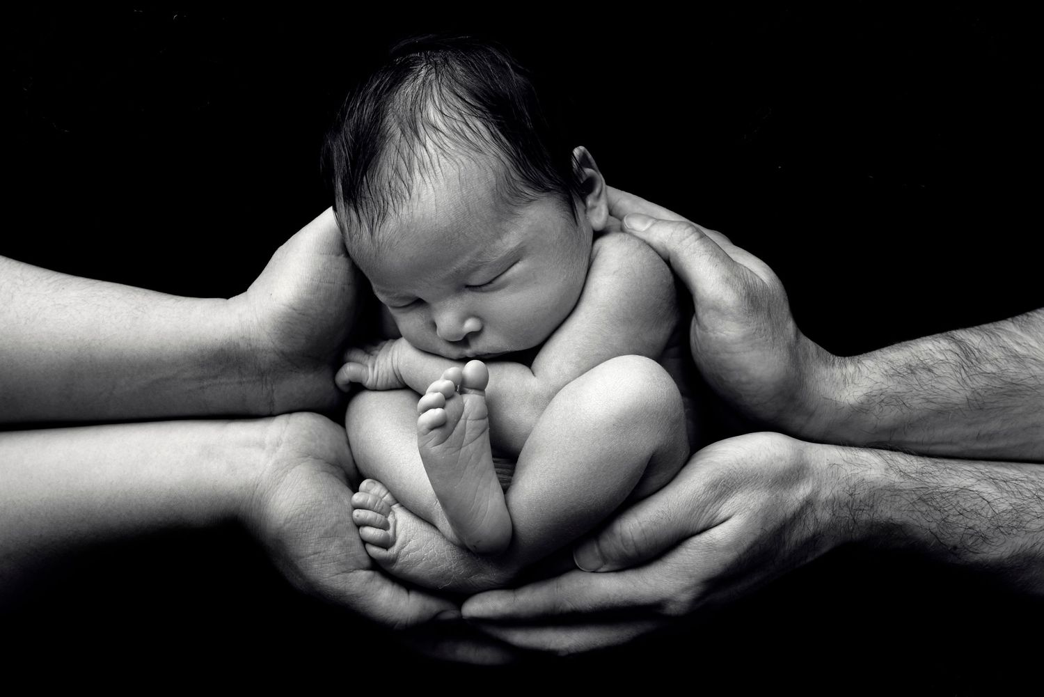 A black and white portrait of a tiny newborn cradled in gentle hands.