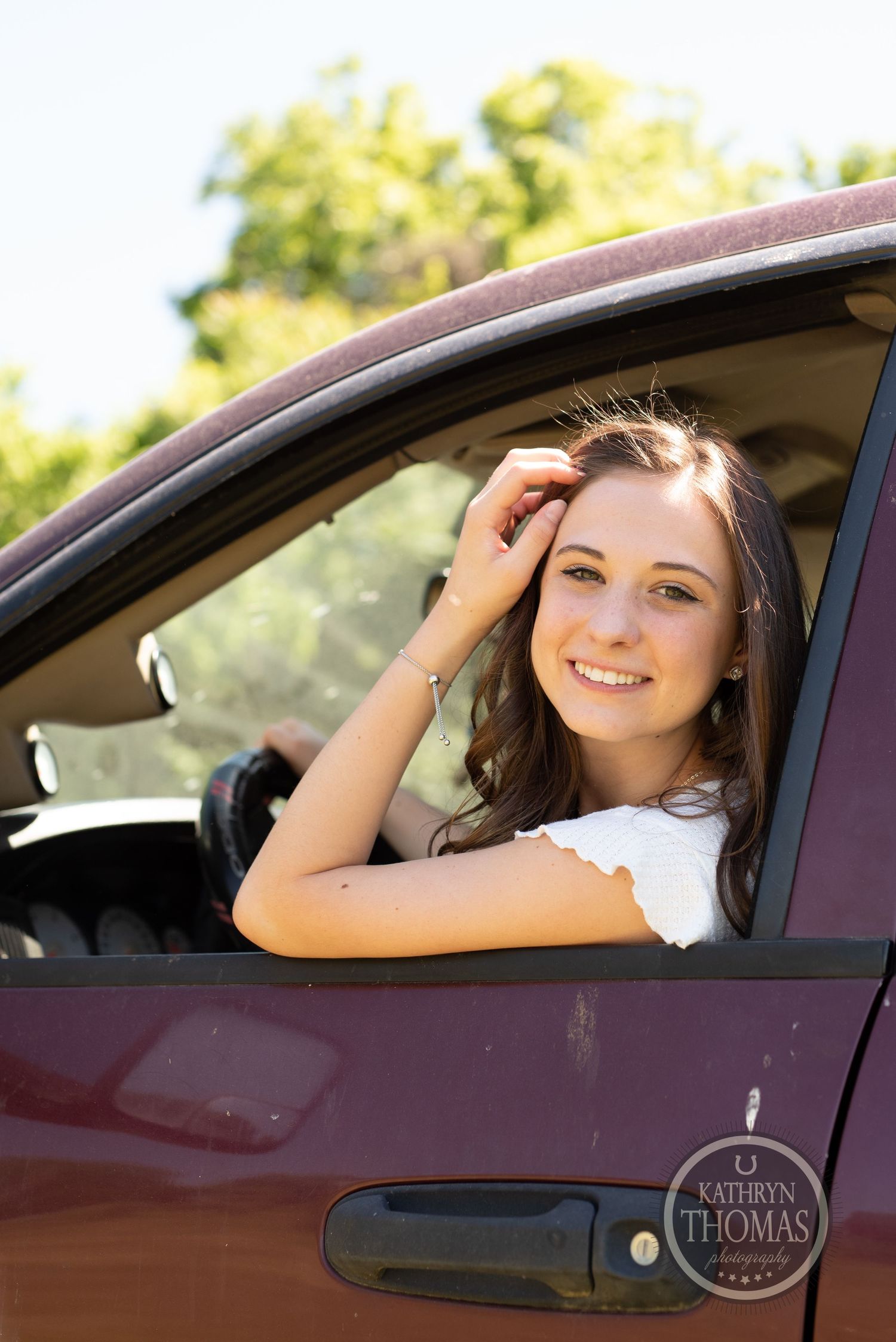 Person smiles while seated in red pickup truck during outdoor photo session.