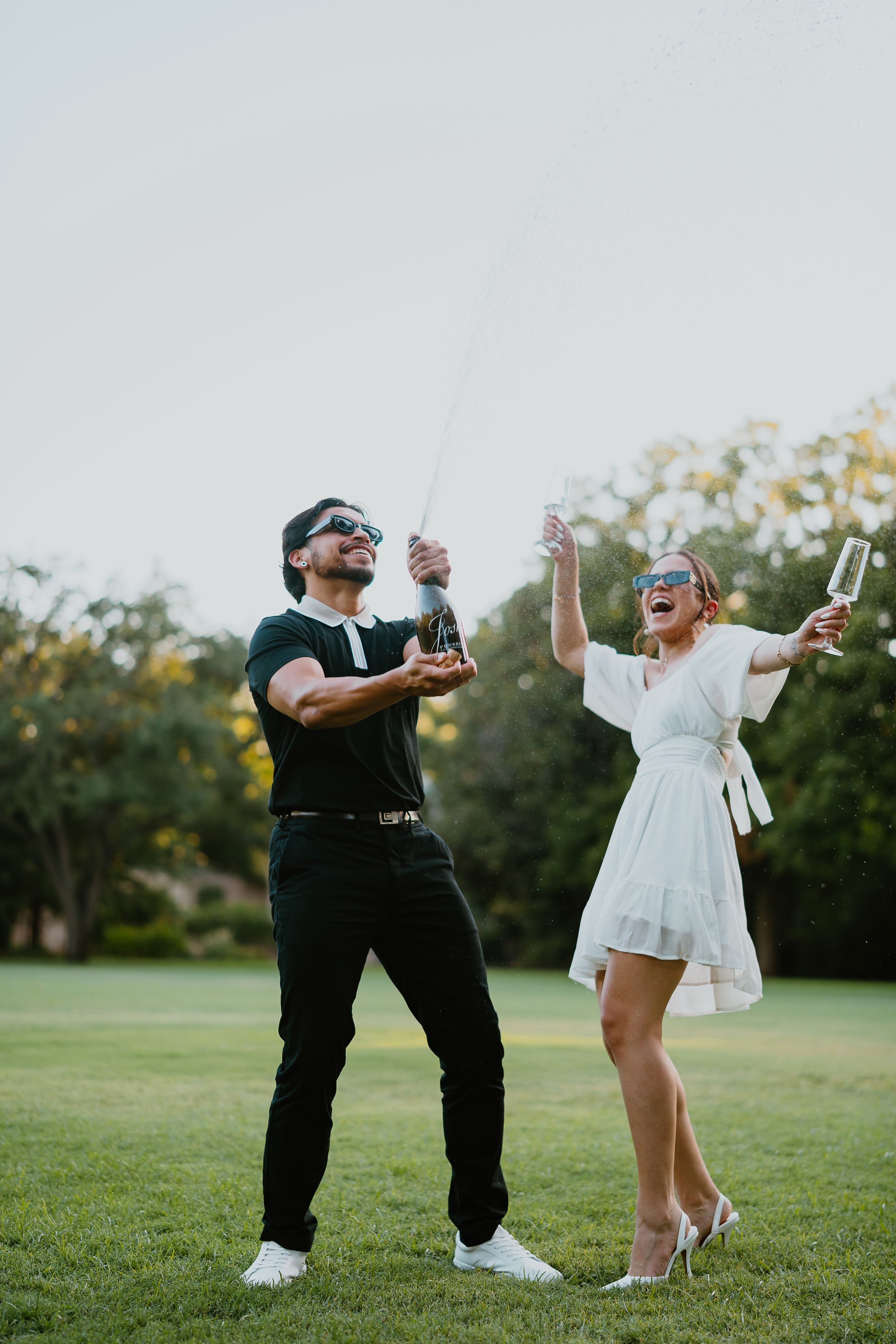 engaged couple pops champagne during engagement photoshoot in highland park texas. alex marie photography.