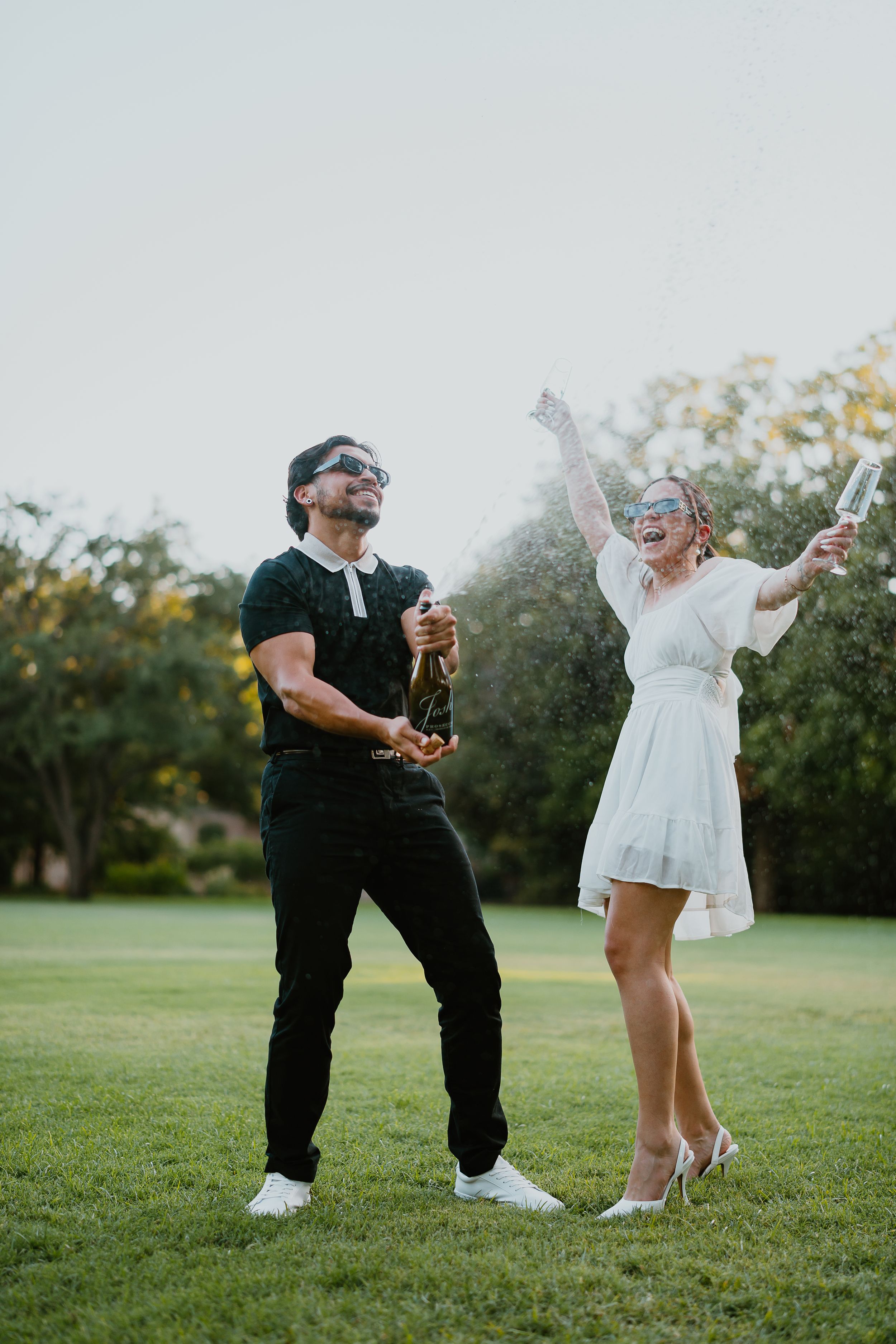 engaged couple pops champagne outside in highland park texas. alex marie photography.