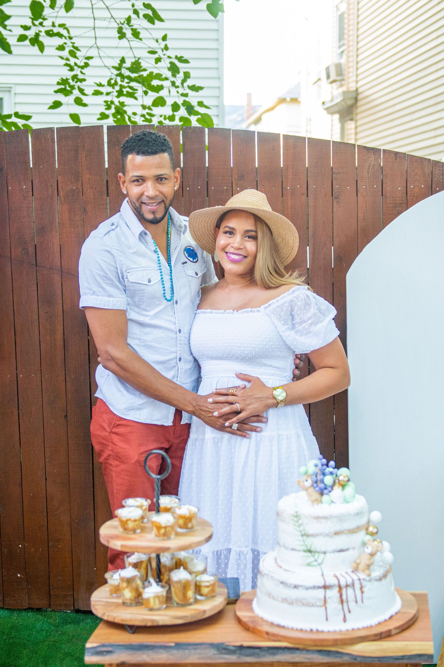 Outdoor baby shower setup with dessert table, balloons and wooden fence backdrop.