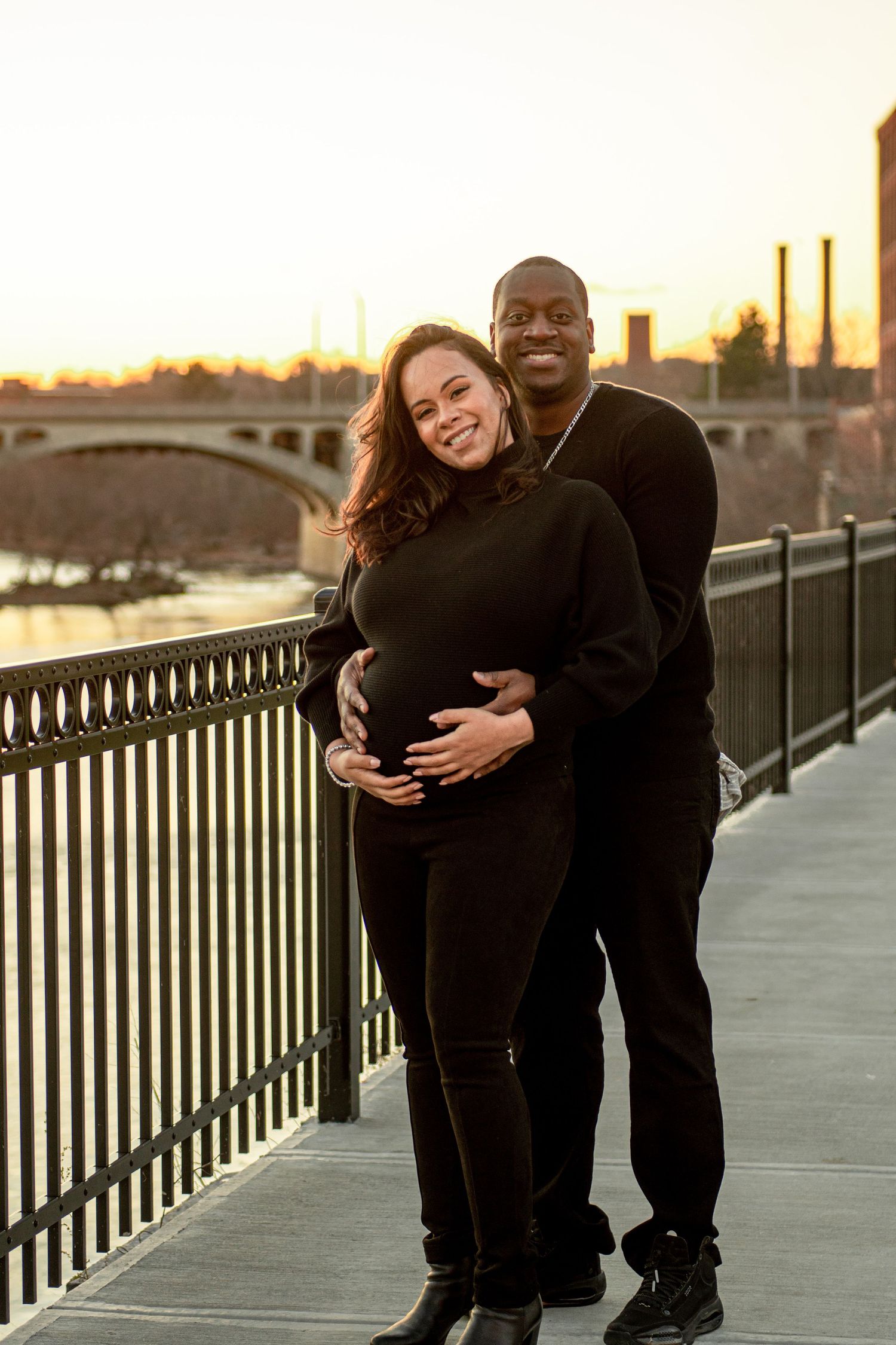 A couple shares an intimate moment on a bridge during sunset for their maternity photos.