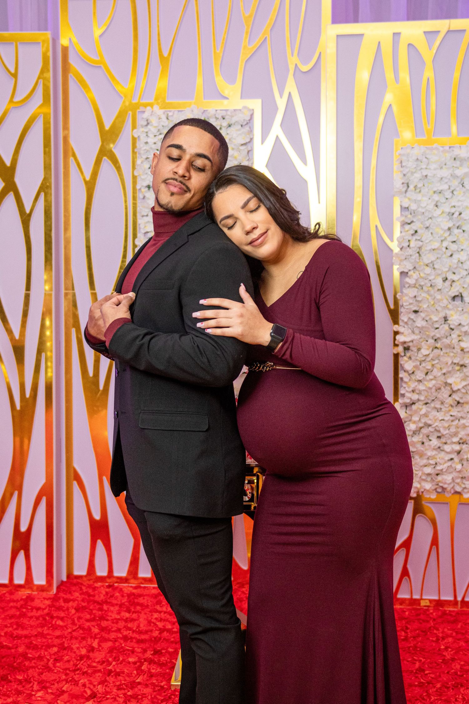 A couple poses playfully against a geometric backdrop during their maternity photoshoot.
