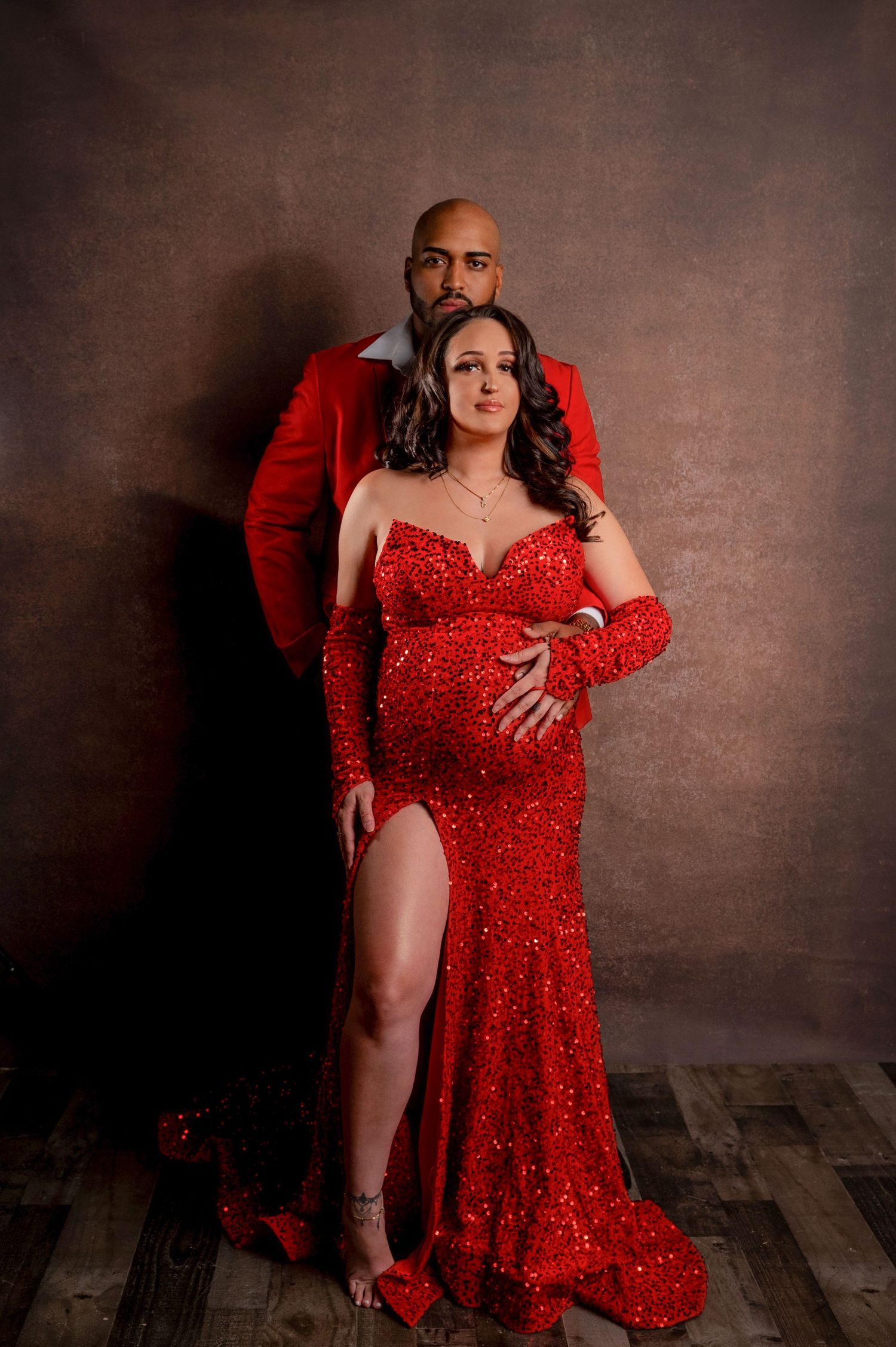 Intimate studio portrait of couple in coordinating red formal attire against dark backdrop.