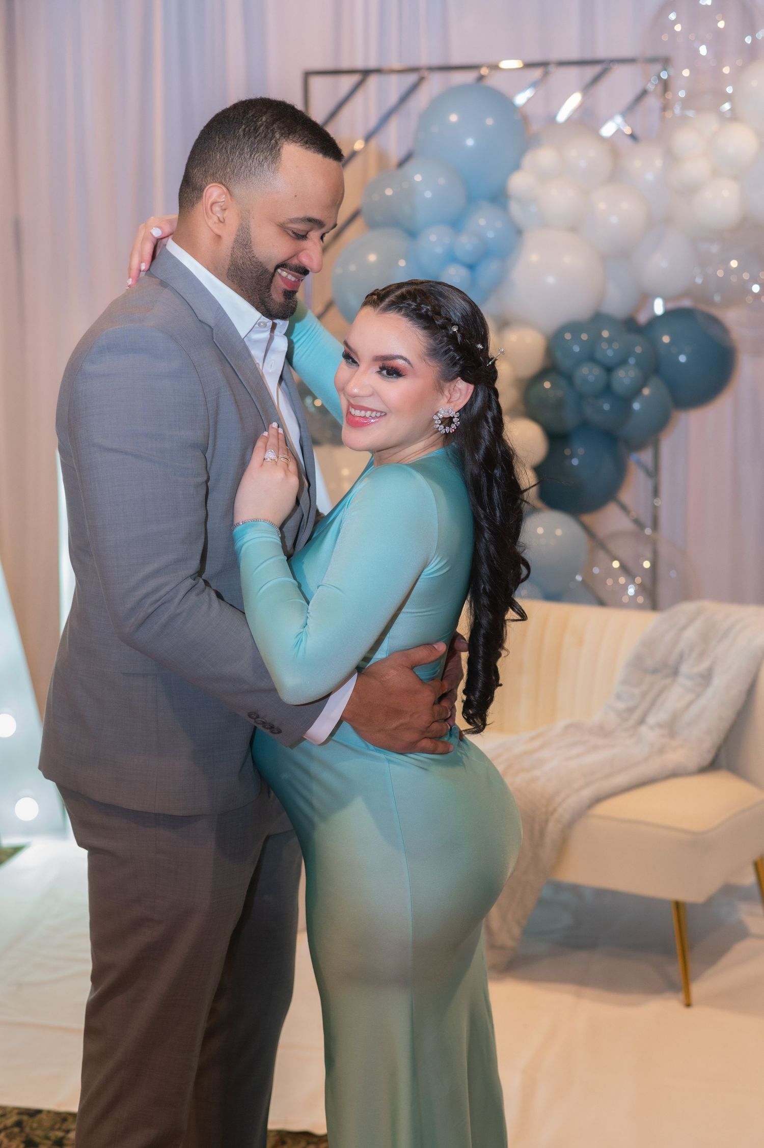 Elegant couple embracing at a baby shower with blue and white balloon decorations.