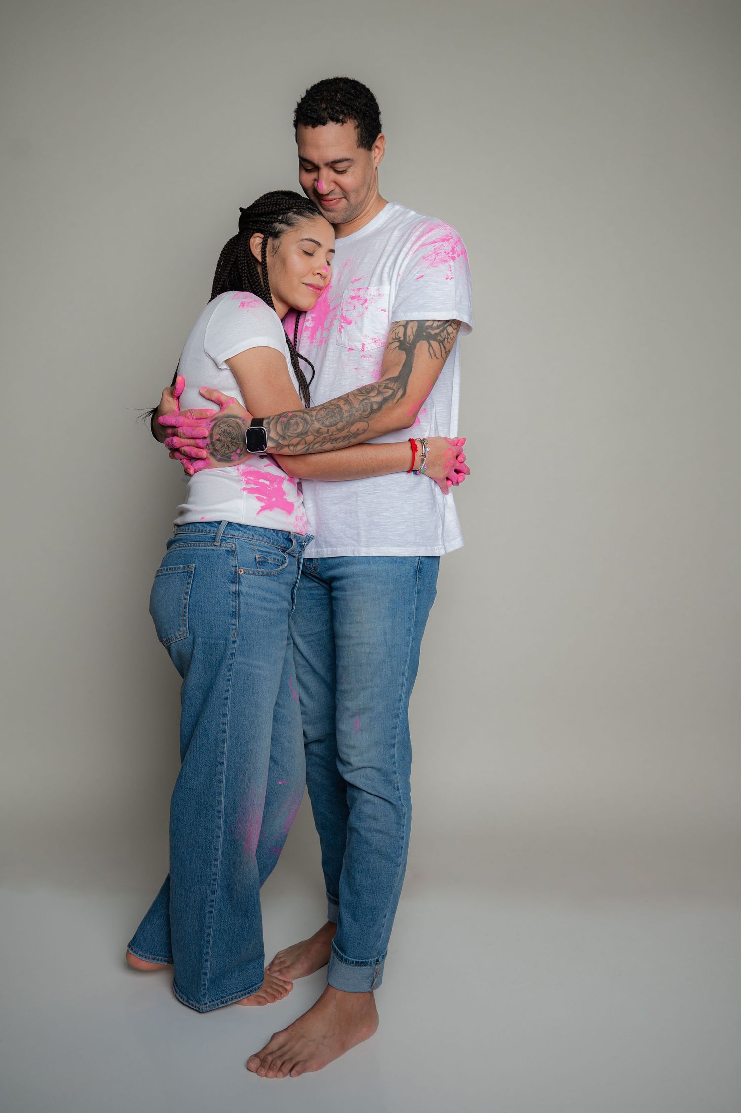 A couple in pink-splattered white t-shirts embraces in a studio setting.