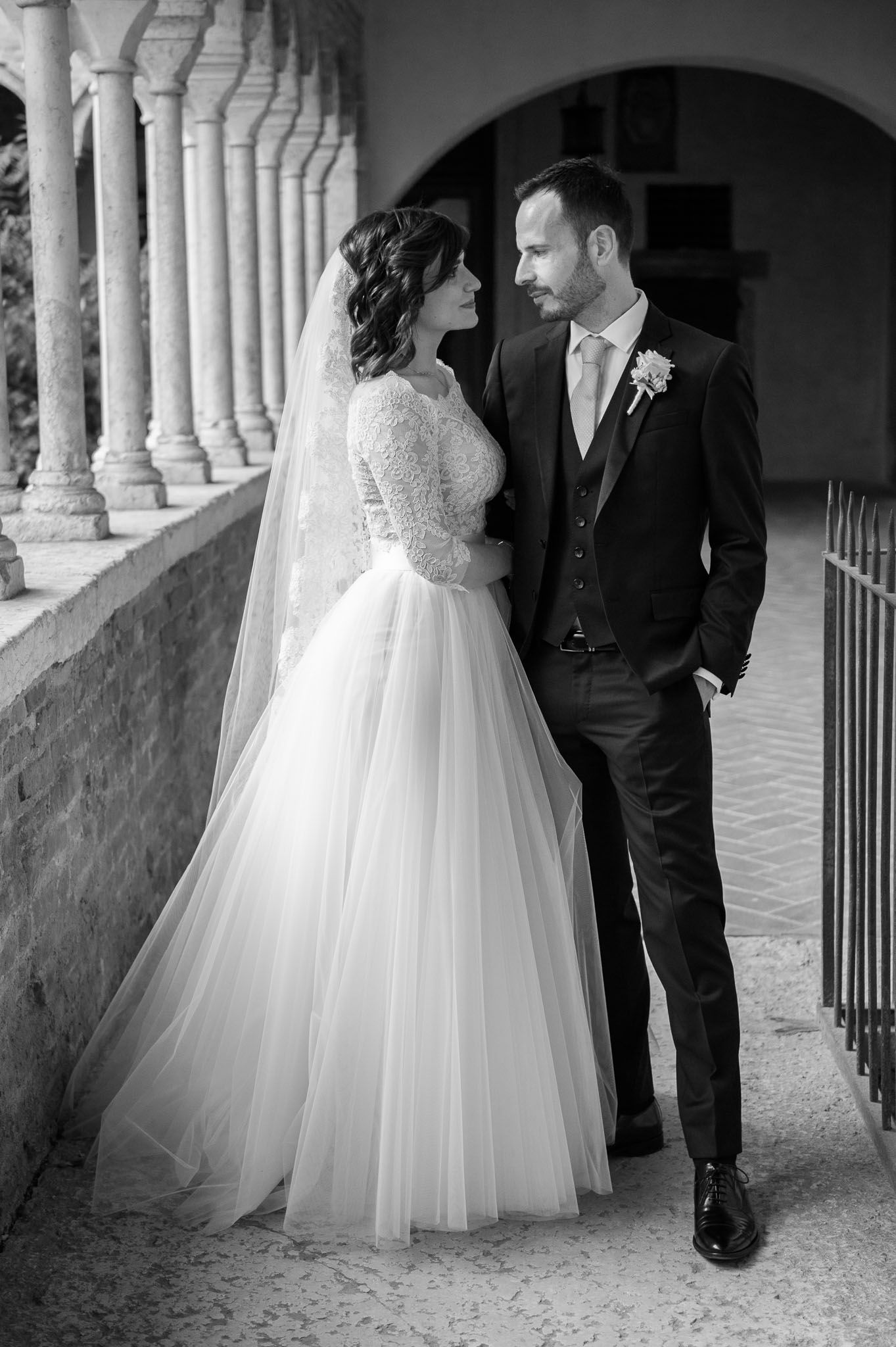 Black and white portrait of newlyweds standing along a colonnade with classic architecture.