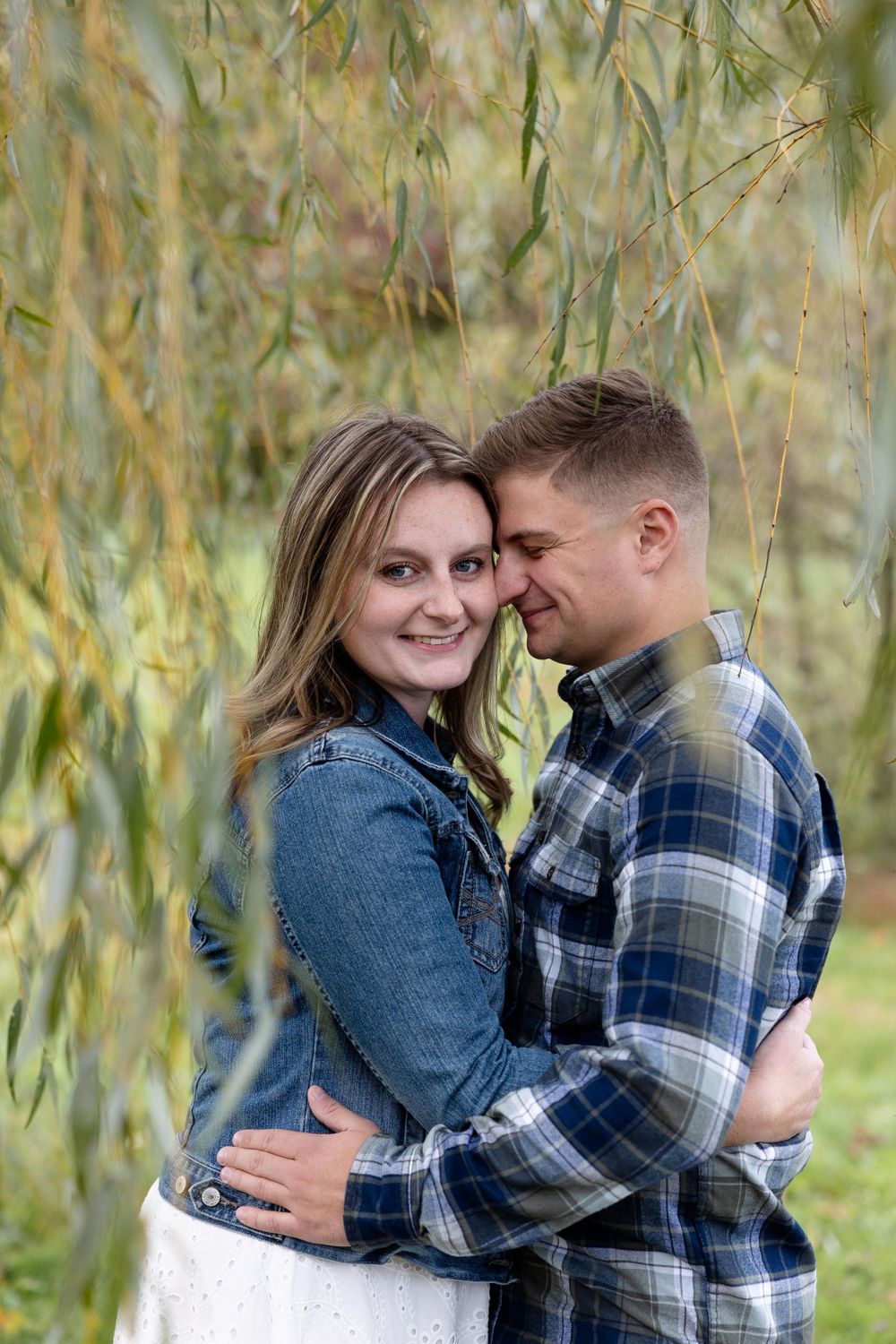 Couple embracing under willow branches during a fall engagement photoshoot.