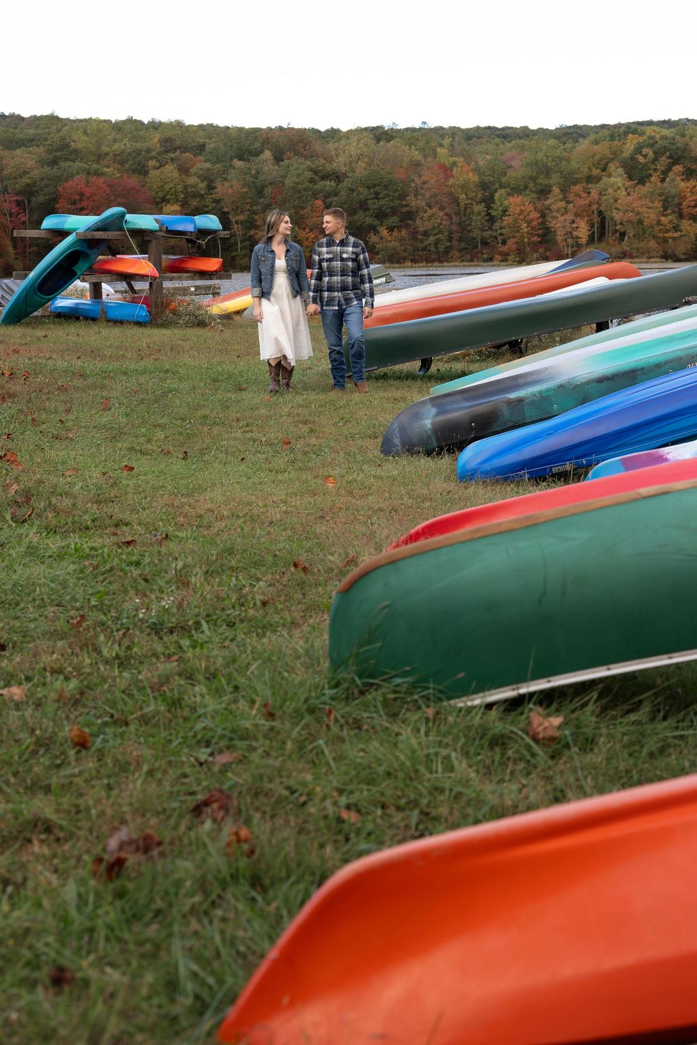 Colorful kayaks line a grassy hillside during fall with a couple standing among them.
