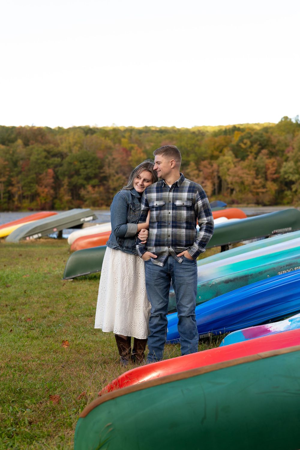 A couple stands close together among vibrant kayaks on an autumn hillside.