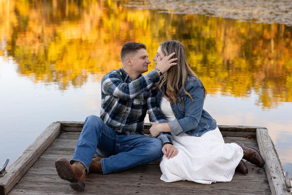 A romantic moment shared on a wooden dock with fall colors reflecting in the water.