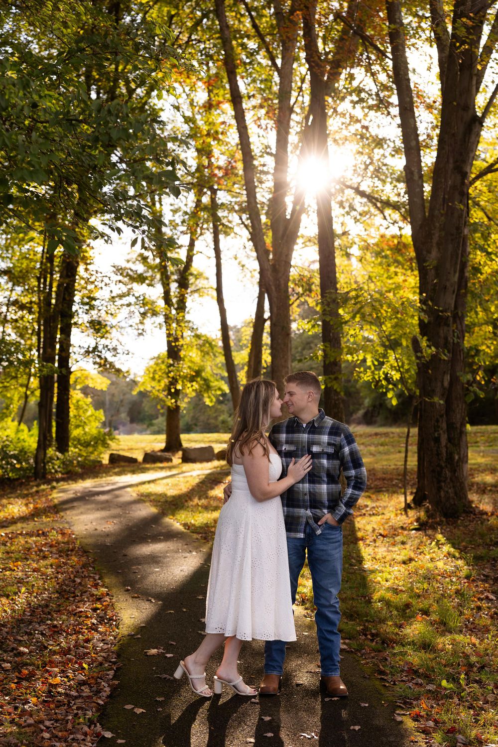 A romantic moment captured on a sunlit path surrounded by golden fall foliage.