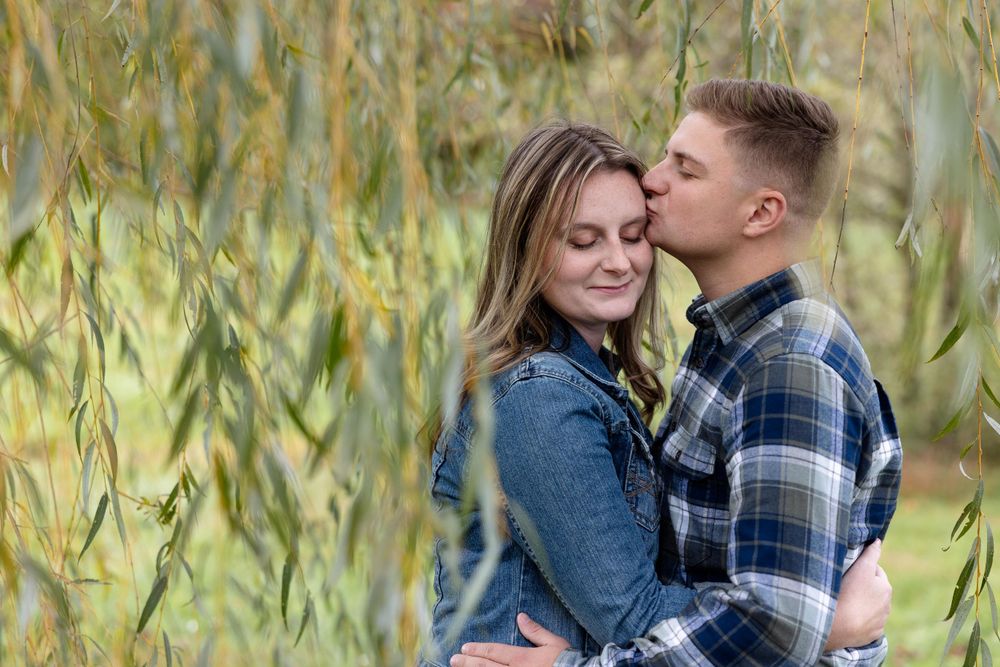 Intimate moment between couple framed by willow tree branches during autumn.