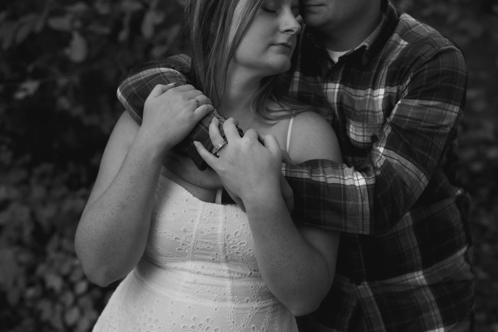 Black and white intimate portrait of couple in plaid shirt and white dress.