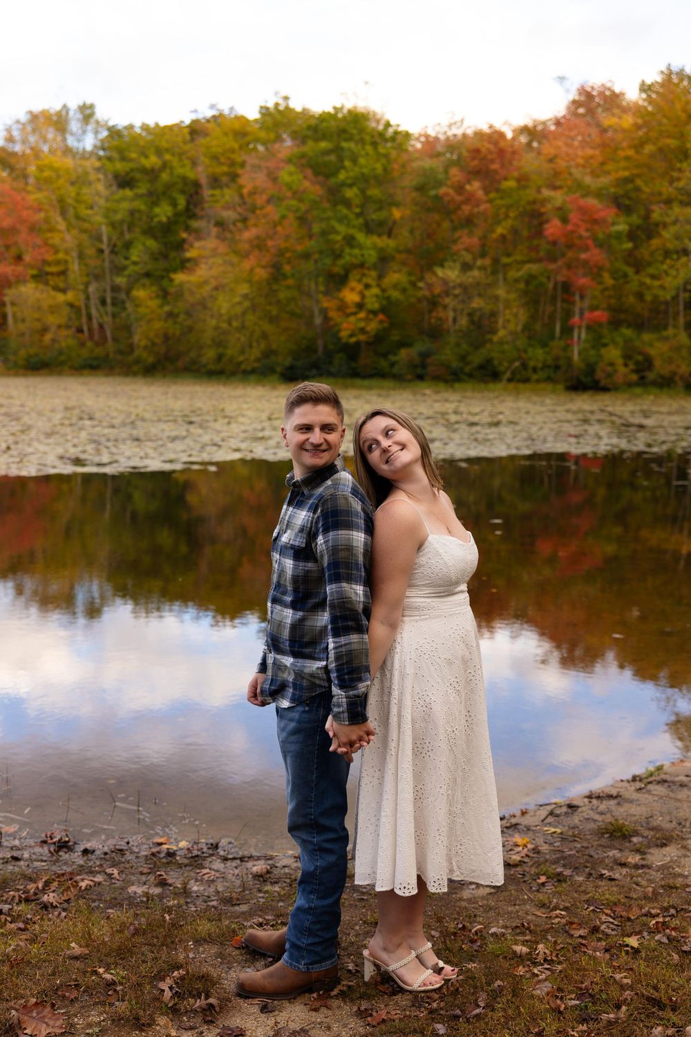 Fall engagement photo by lake with vibrant autumn colors in background.