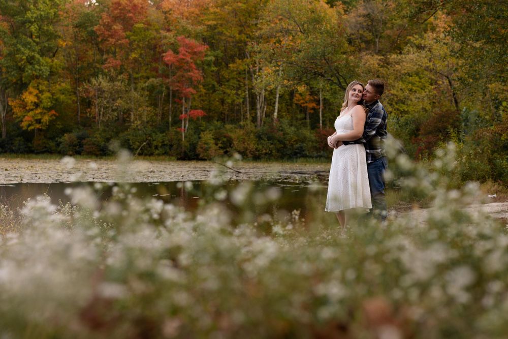 Romantic couple portrait through wildflowers with fall foliage and lake backdrop.