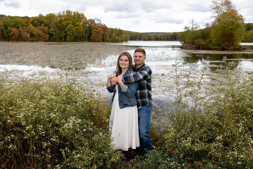 Engagement photo of couple by autumn lake surrounded by fall colors.