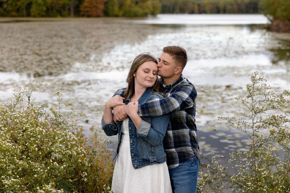 Romantic lakeside moment with couple embracing against water backdrop.