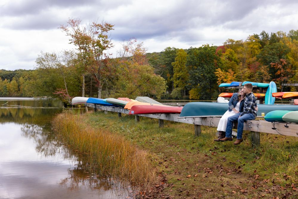 Colorful kayaks line the shore of an autumn lake with fall foliage reflecting in the water.