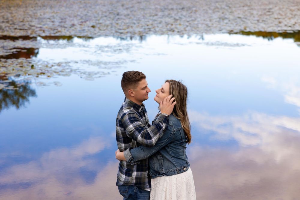 Intimate lakeside engagement photo with couple against reflective water background.