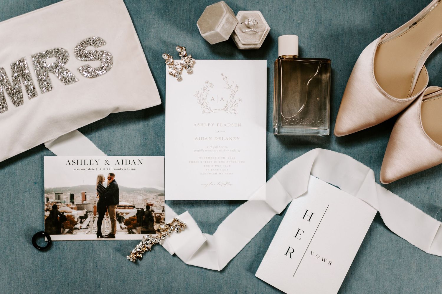 Elegant wedding details including invitations, rings, and accessories arranged on teal fabric.