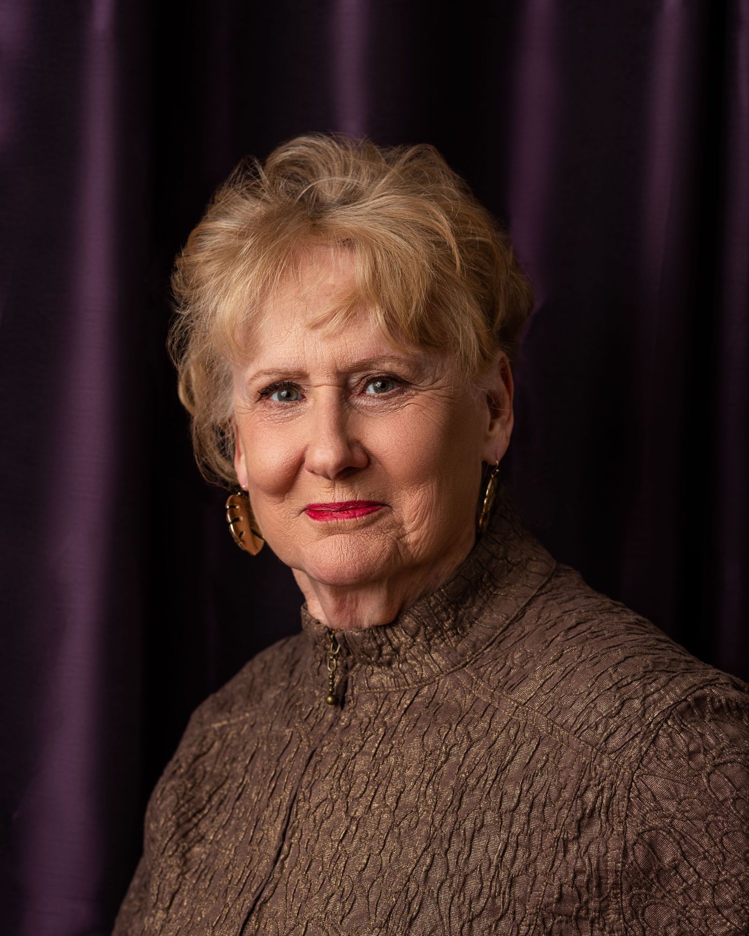 Classic portrait against purple backdrop featuring someone in brown knit sweater.