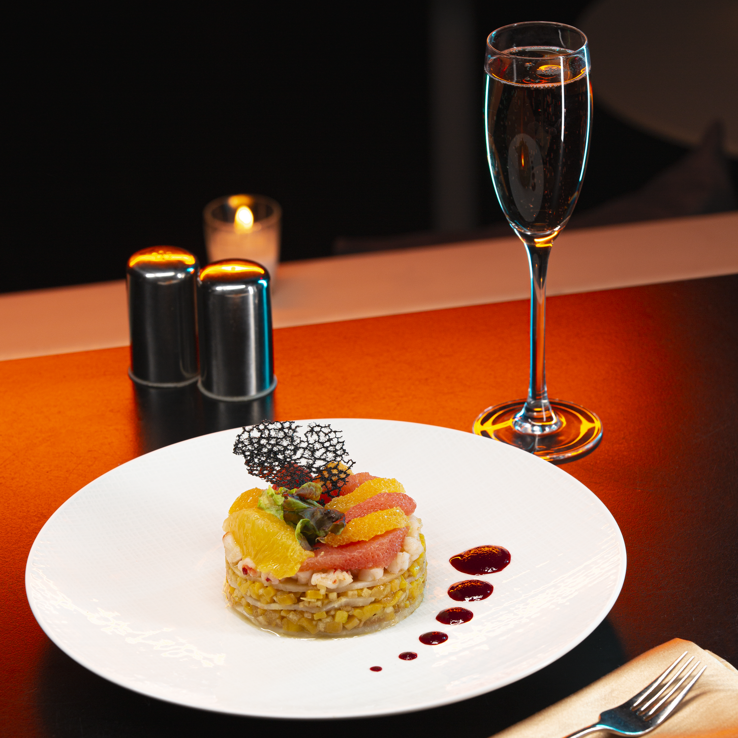 Elegant plated dish with yellow garnish served alongside a glass of champagne on dark table setting.