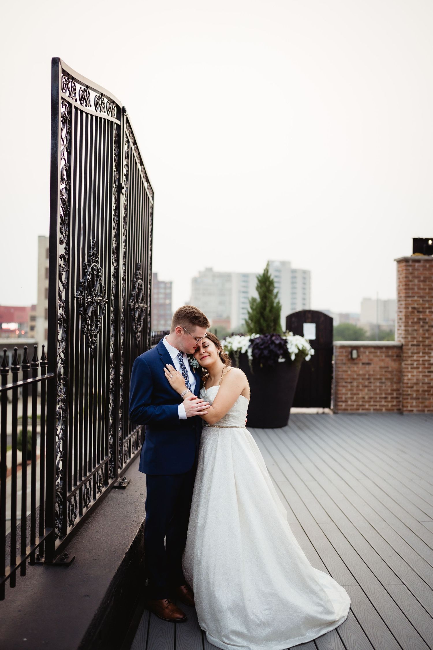 Couple shares intimate moment on rooftop deck near ornate iron gates.