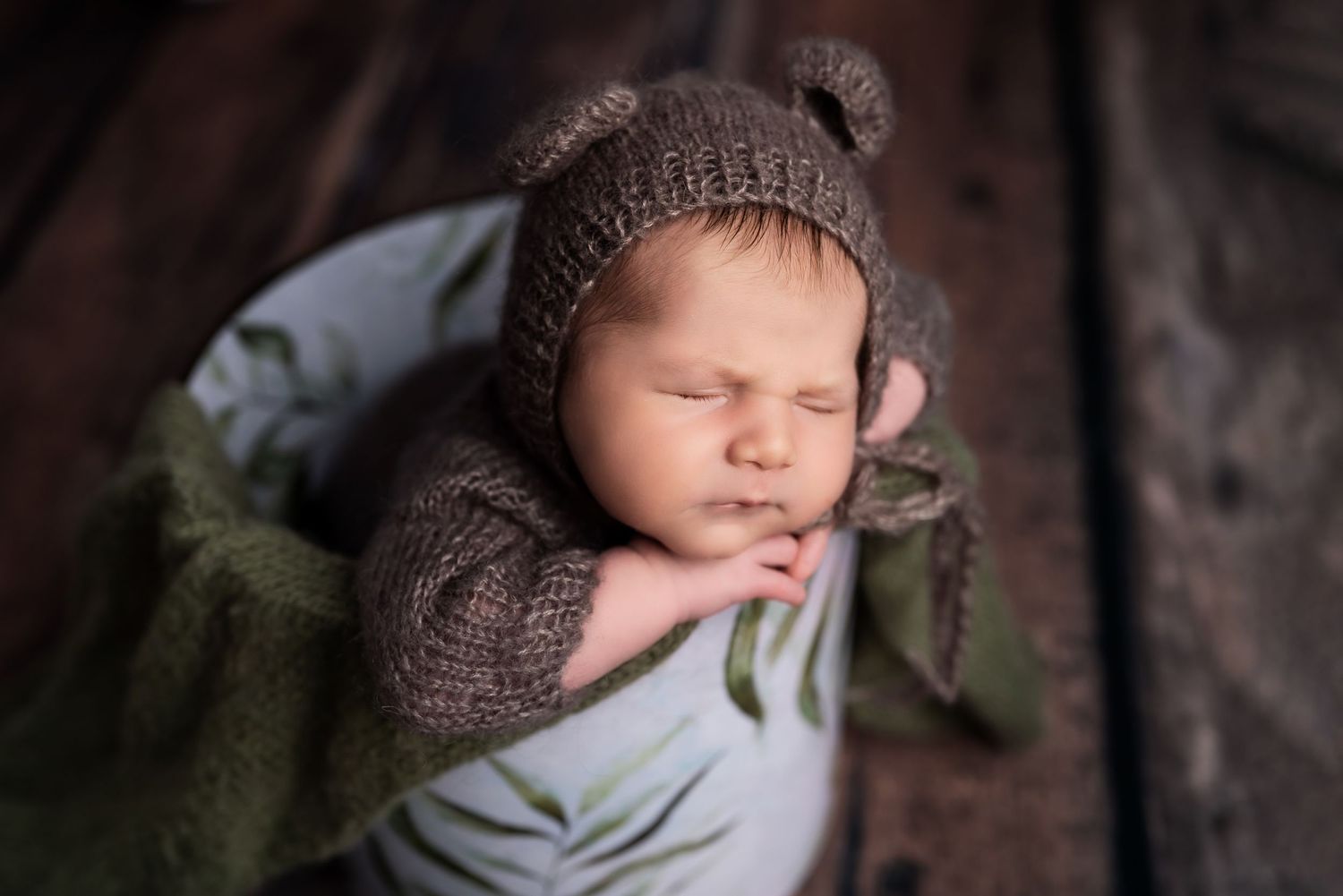 Baby wearing knitted brown hat sleeping on dark textured surface.