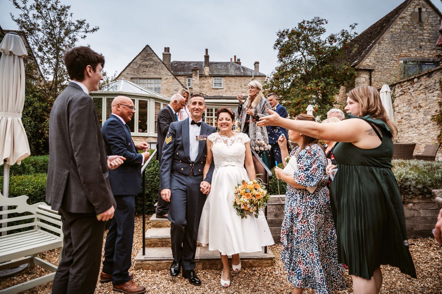 Wedding party celebrating on a stone patio surrounded by historic buildings and autumn foliage.