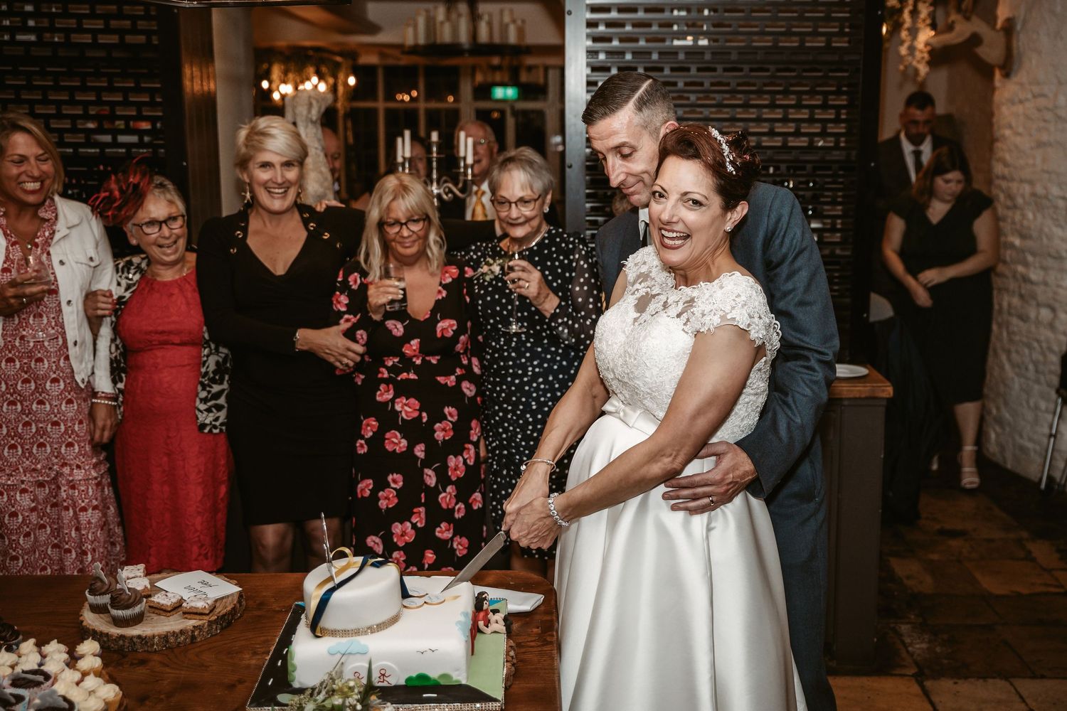 Newlyweds cutting their wedding cake surrounded by smiling guests.