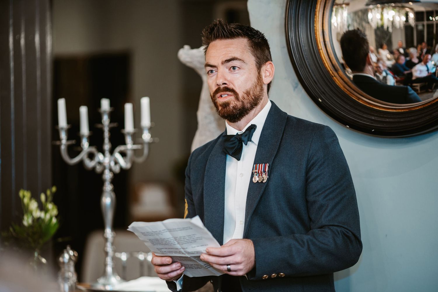 Serviceman in formal military attire delivers a speech at an elegant wedding reception.