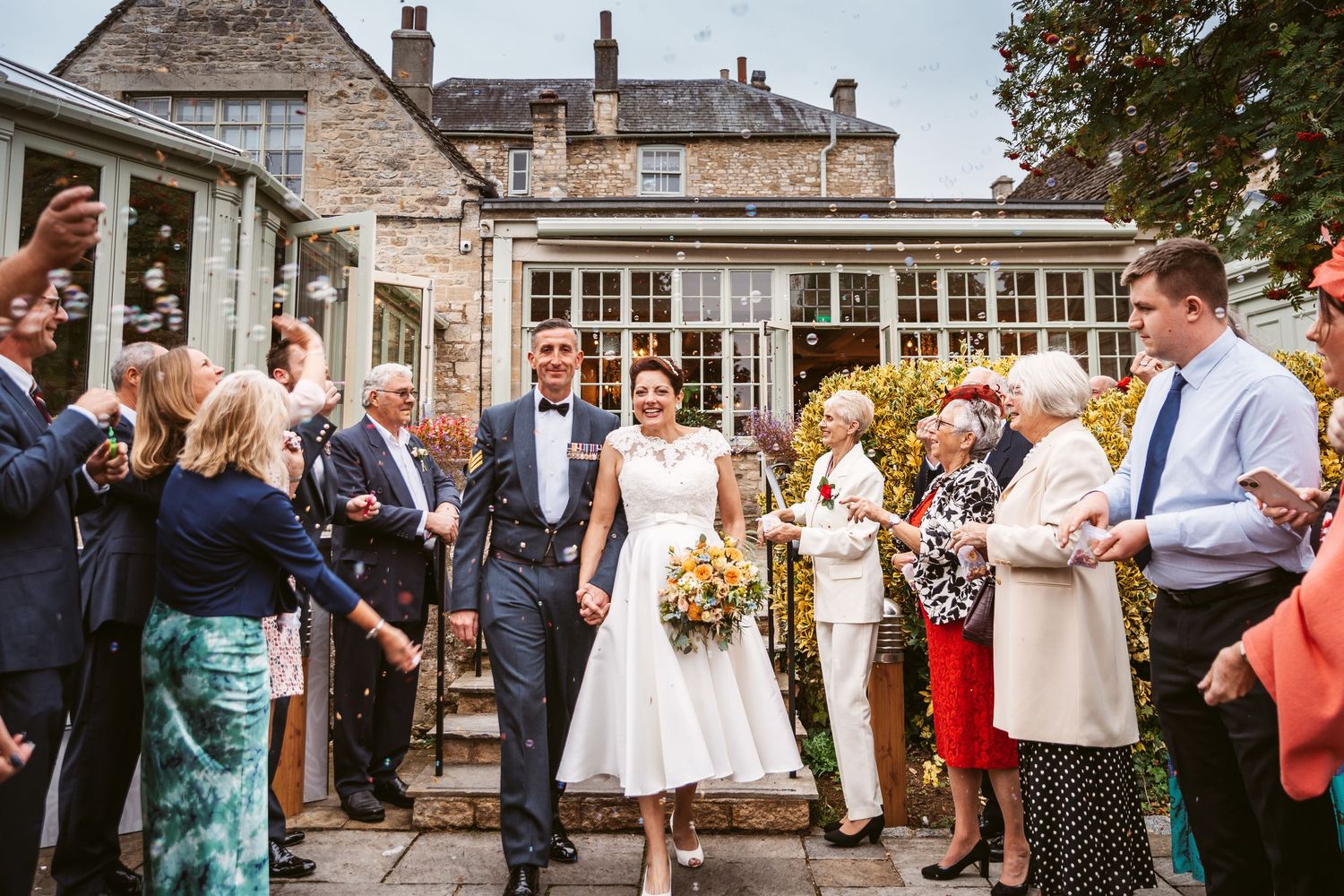 A couple exits their wedding venue while guests line the stone steps to celebrate.