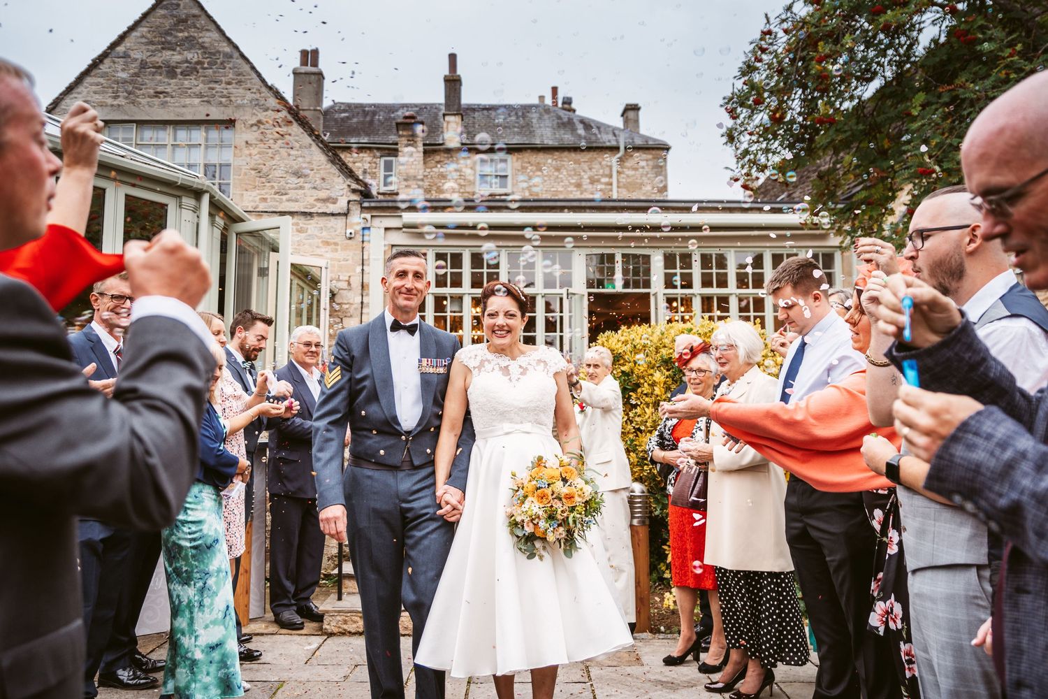 Guests applaud the newlyweds as they walk through the crowd outside a historic stone building.