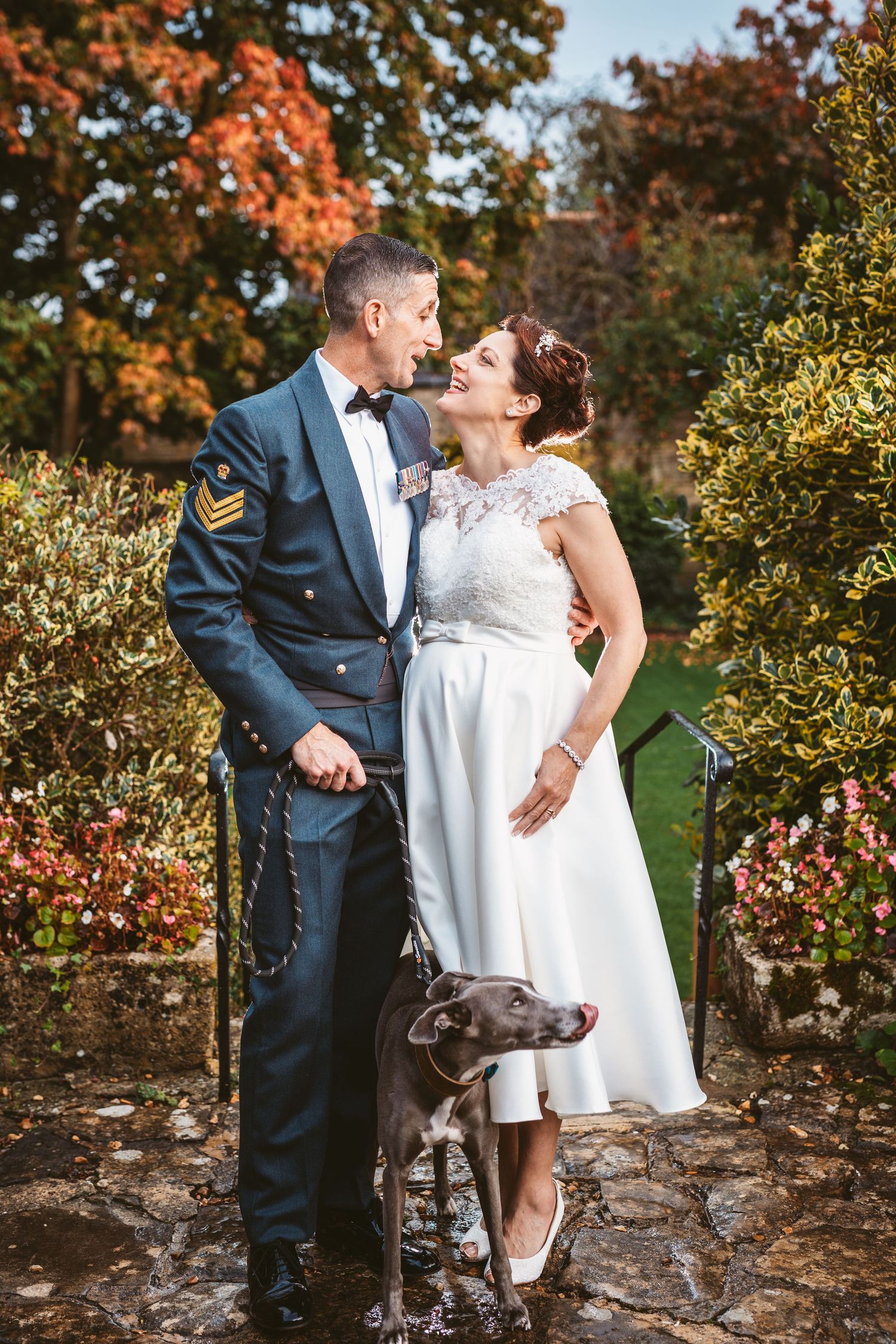 Intimate autumn wedding portrait with military groom and grey dog in garden setting.