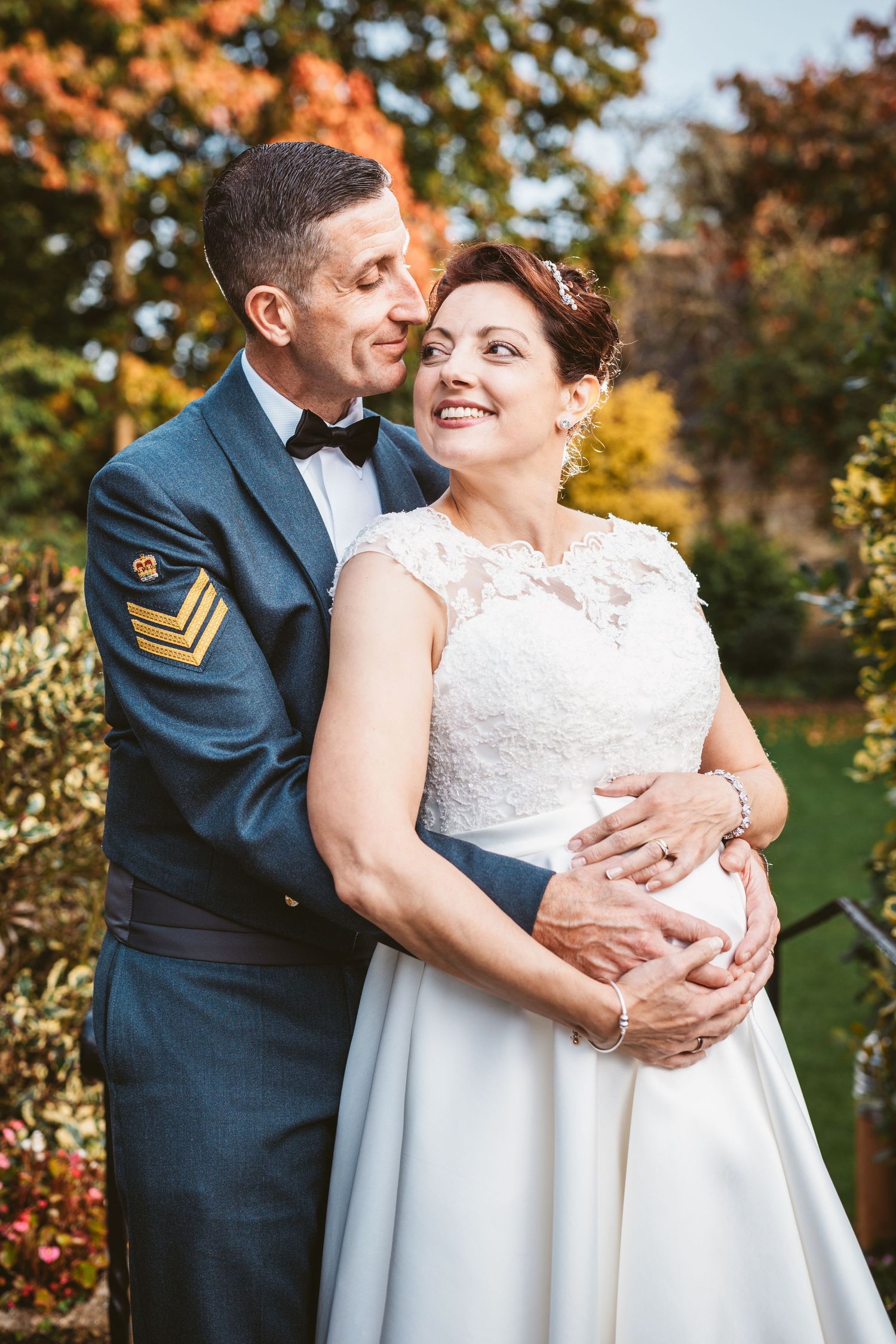 Newlyweds in military uniform and tea length wedding dress share intimate moment in fall garden.