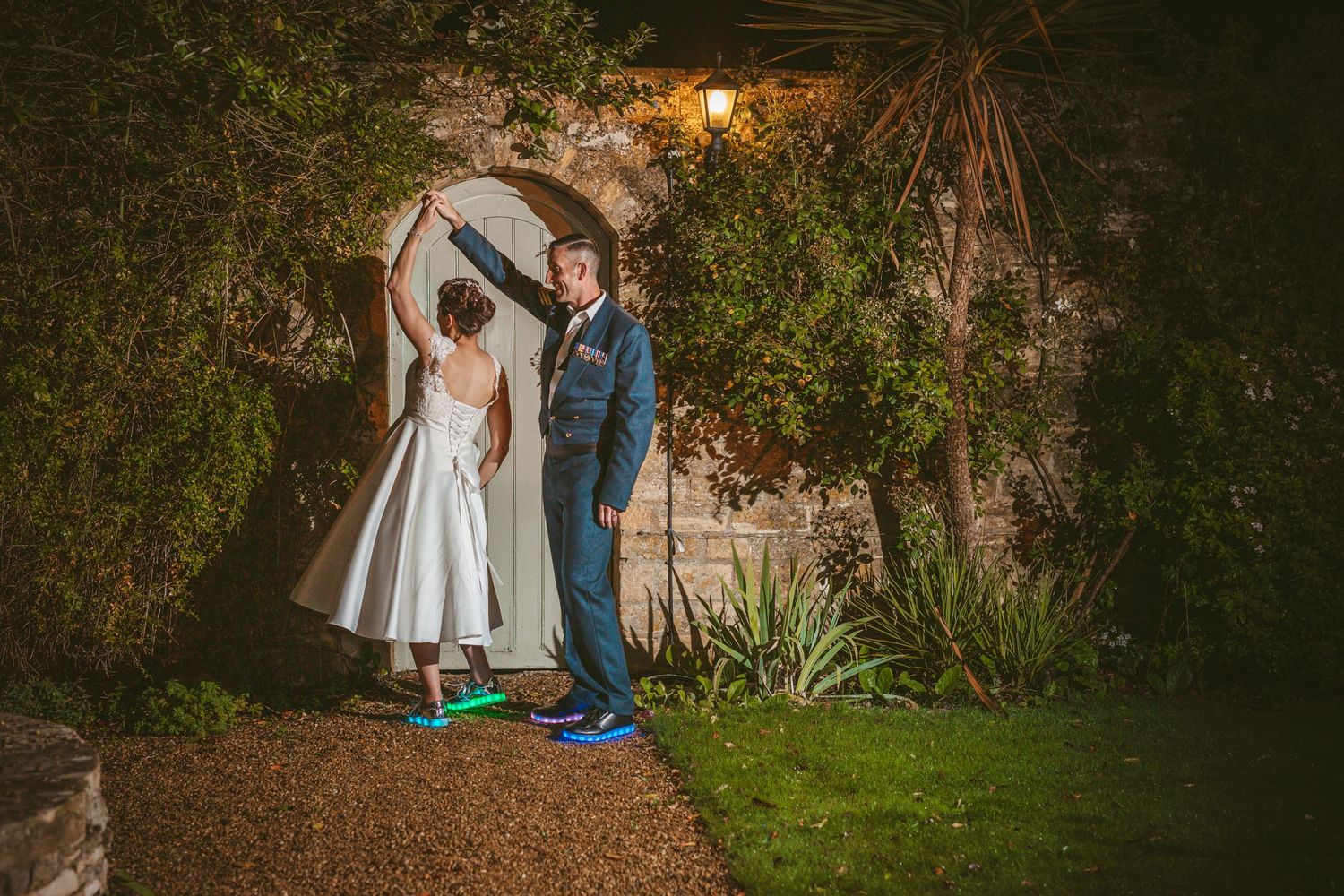 A couple shares a romantic dance pose in front of an illuminated garden archway.