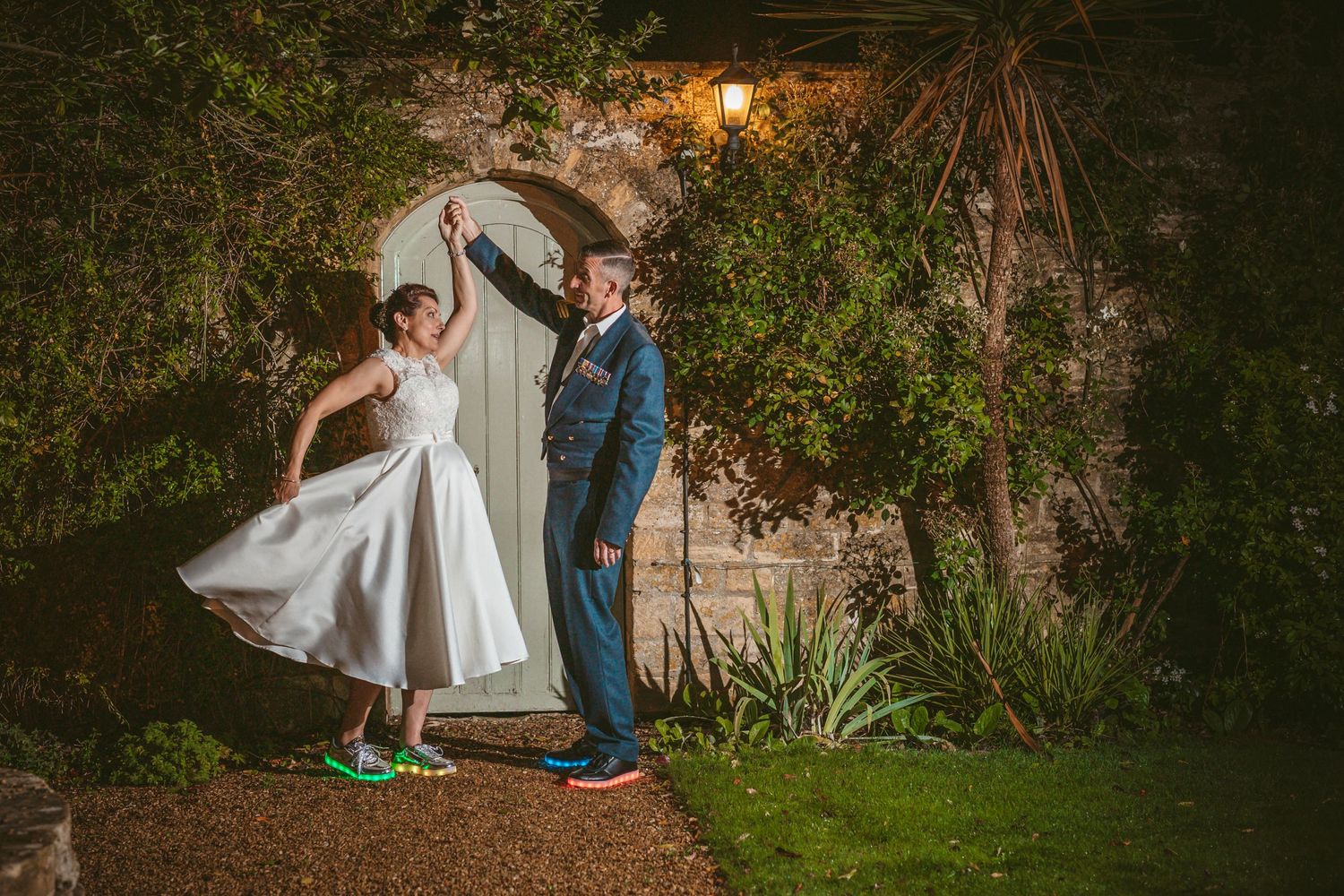 A couple dances and twirls beneath a vine-covered garden archway in the evening.