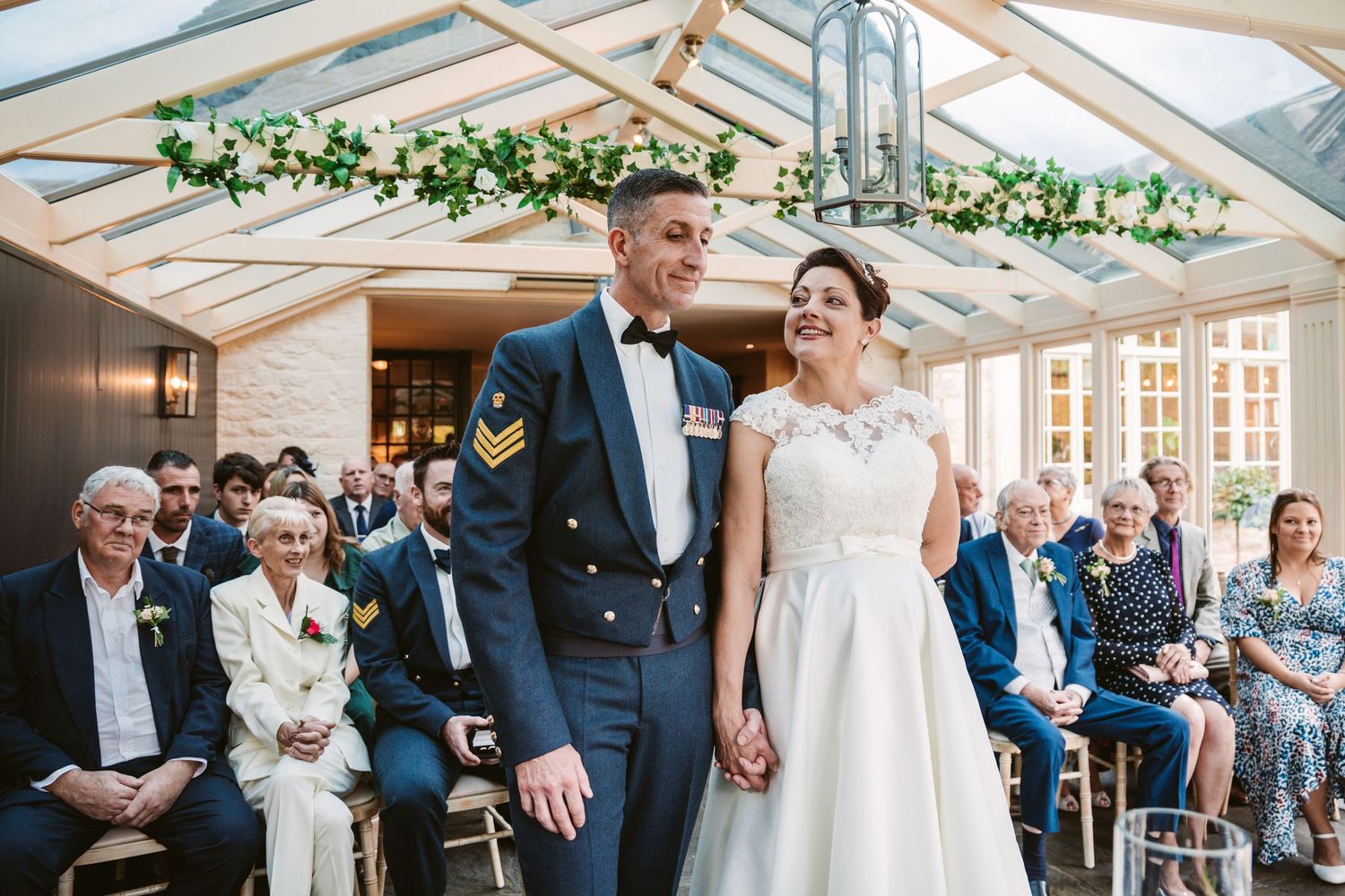 Wedding ceremony in a light-filled conservatory with greenery and white decor.