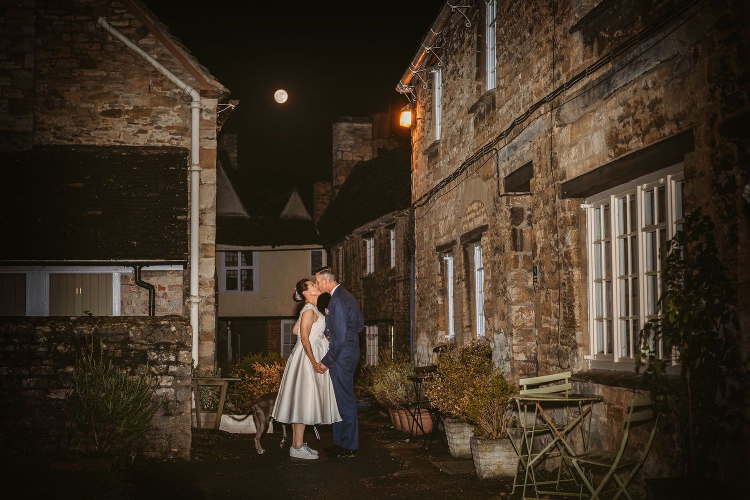 Romantic nighttime portrait of couple outside stone building with warm lighting.