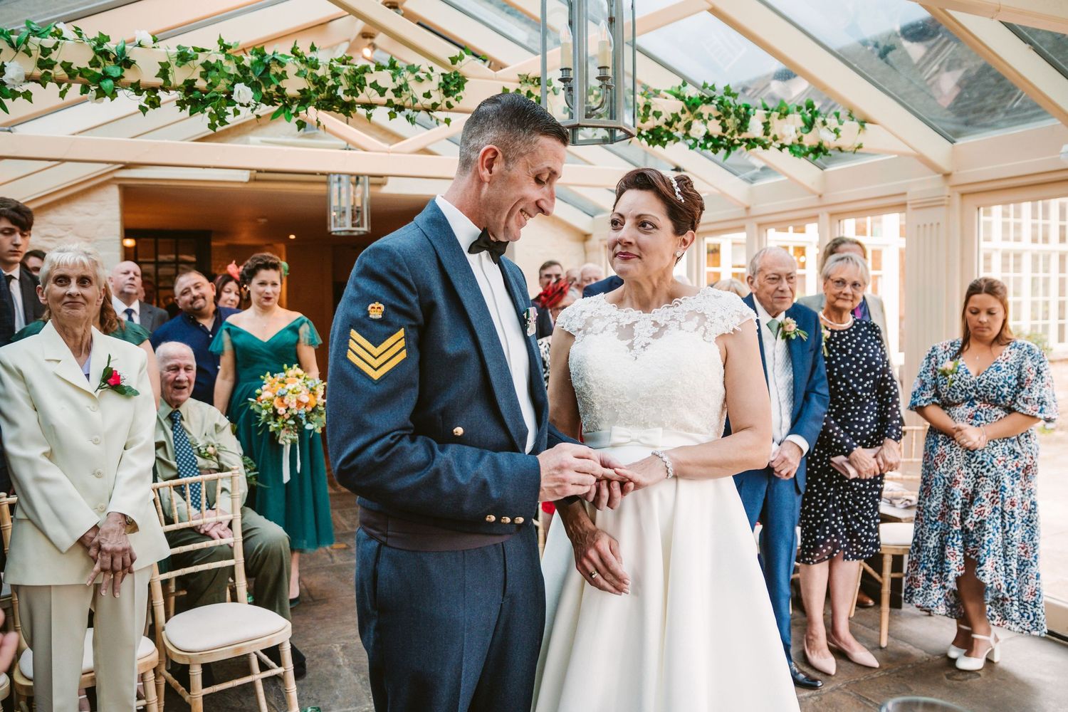 A joyful wedding ceremony in a bright conservatory with elegant greenery decor and guests looking on.