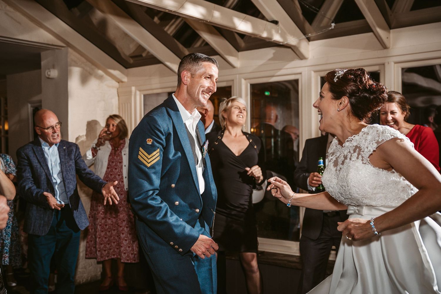 A couple dances and smiles at their wedding reception while guests watch in a rustic venue.