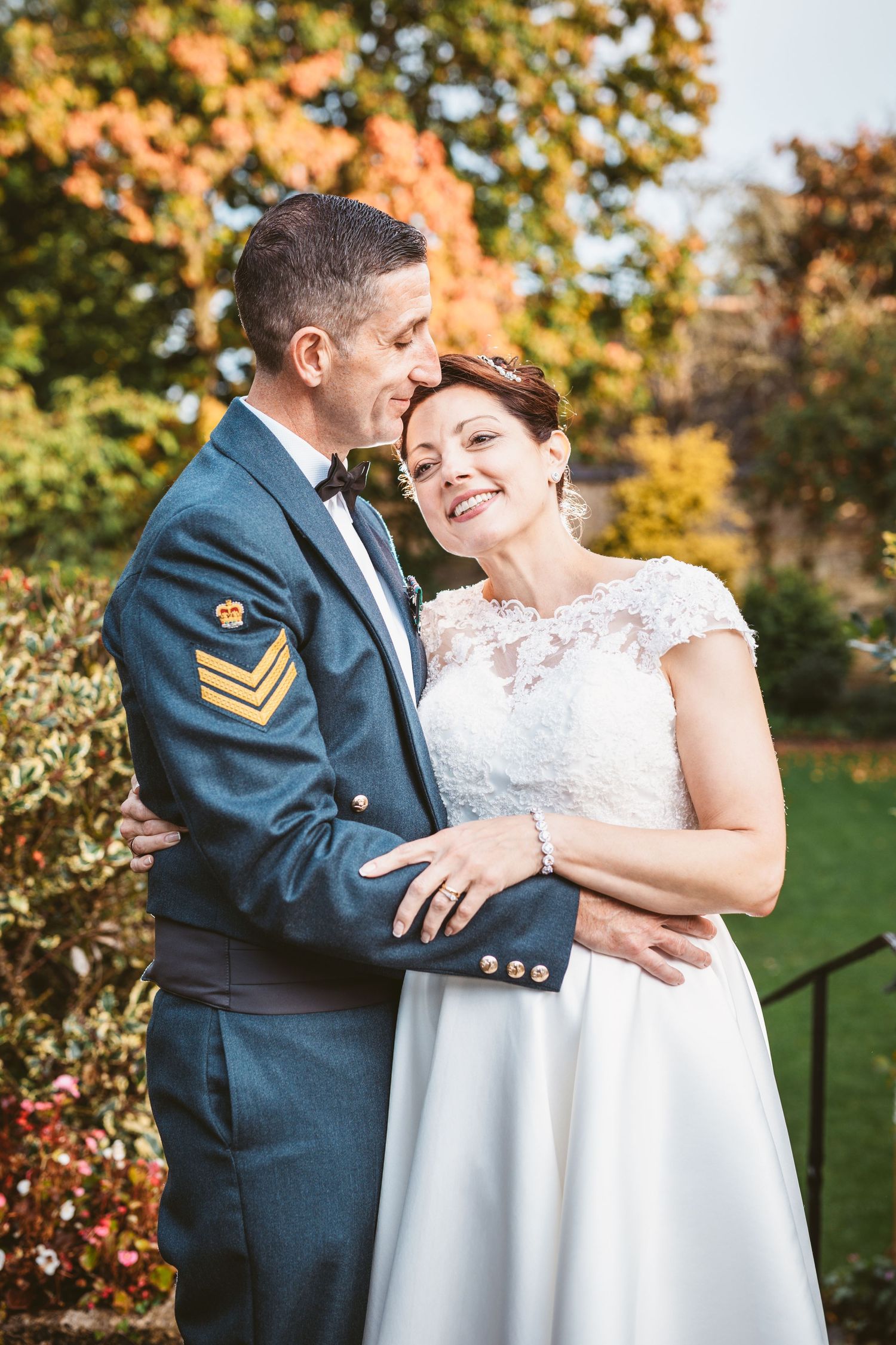 Intimate moment between military groom and bride against autumn garden backdrop.