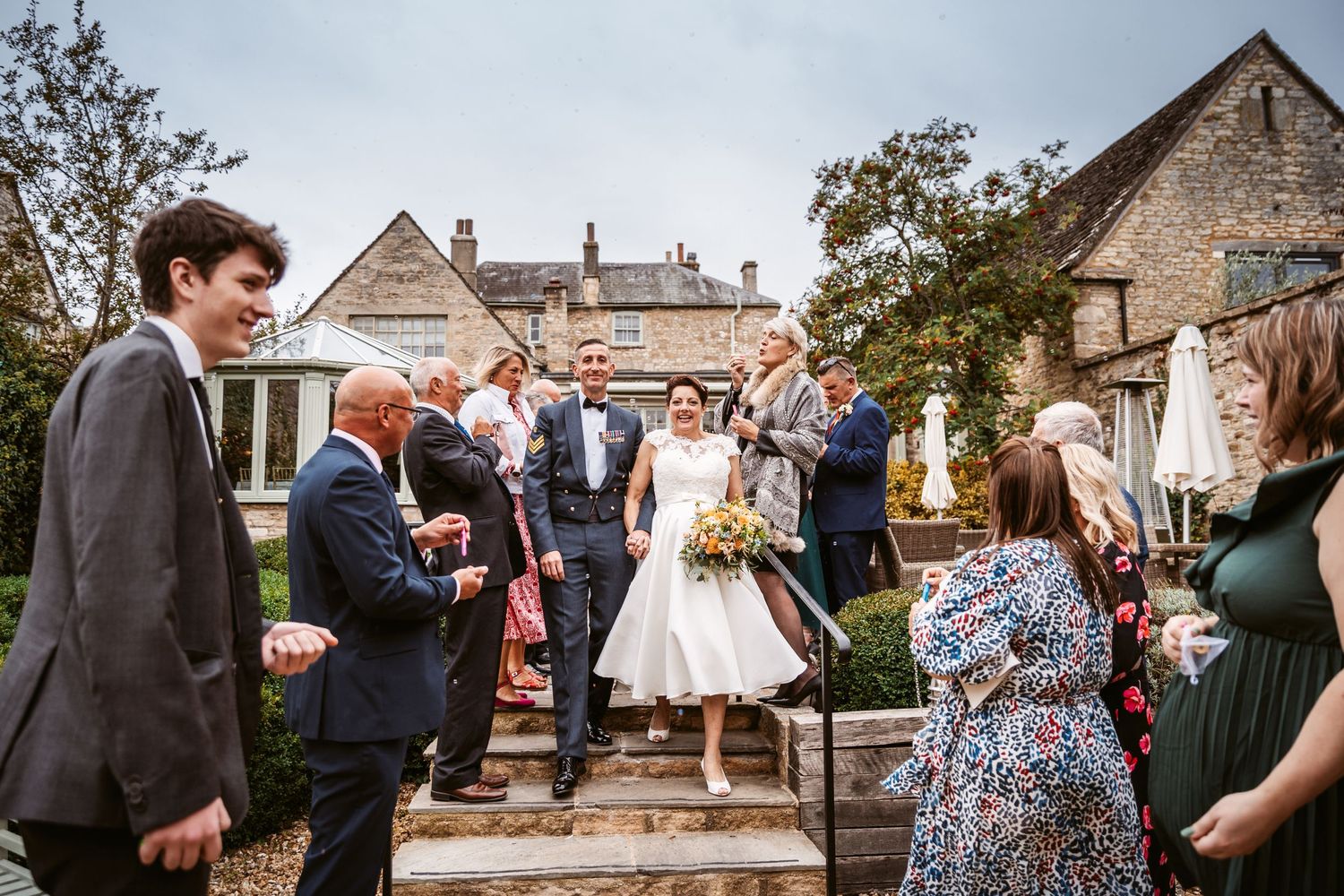 Wedding guests gathered around a couple celebrating on outdoor stone steps with historic buildings in the background.