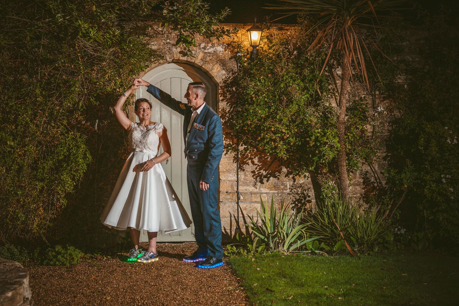 A couple poses playfully in front of an arched garden doorway at night wearing sneakers.