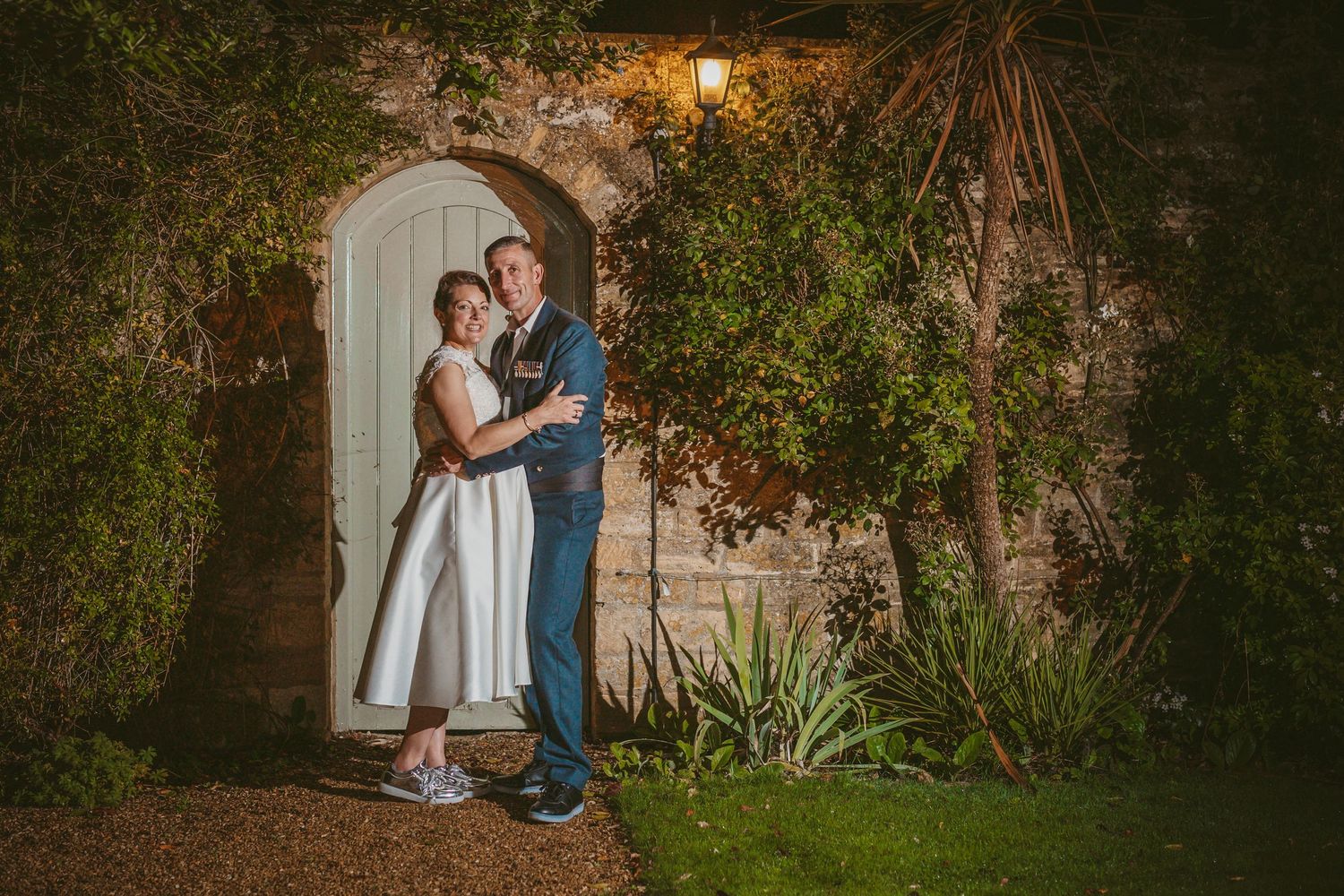 A couple embraces in front of a garden archway while wearing casual sneakers.