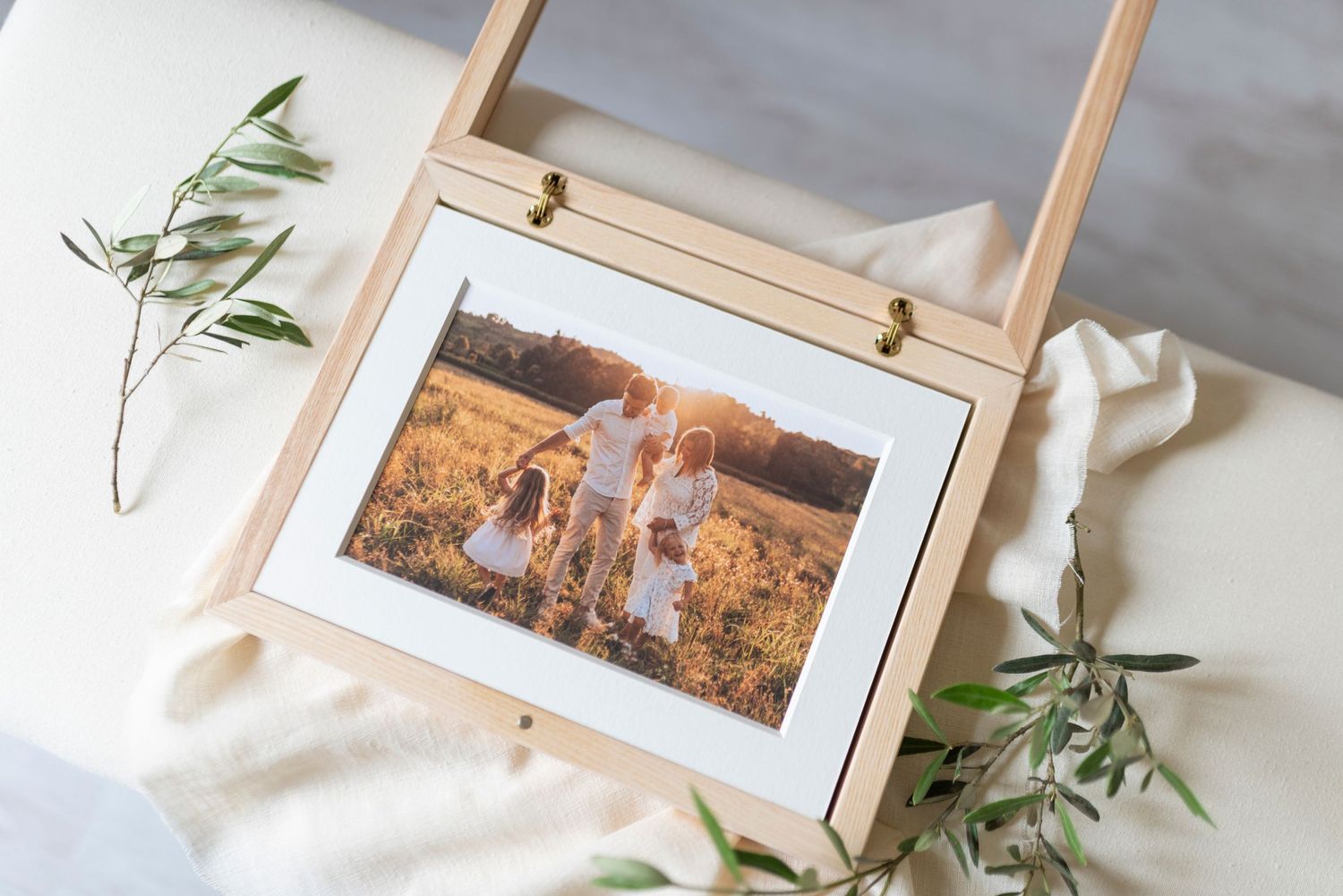 Family portrait photo in a natural wood easel frame surrounded by olive branches on linen.