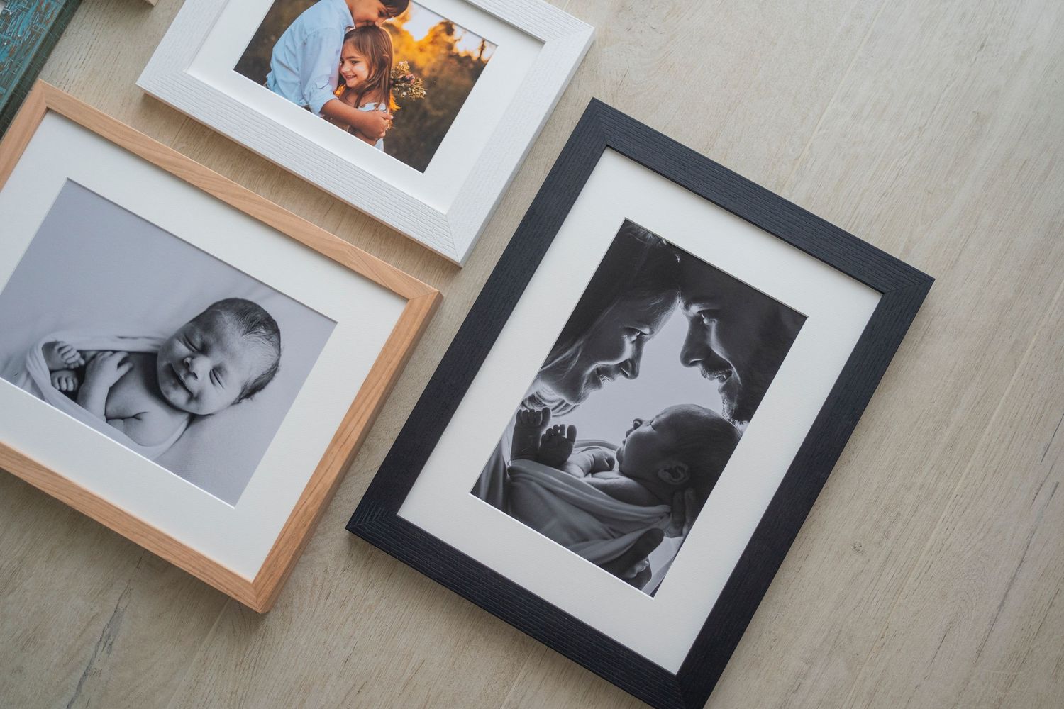 Black and white baby and family photos displayed in natural wood and black frames on a floor.