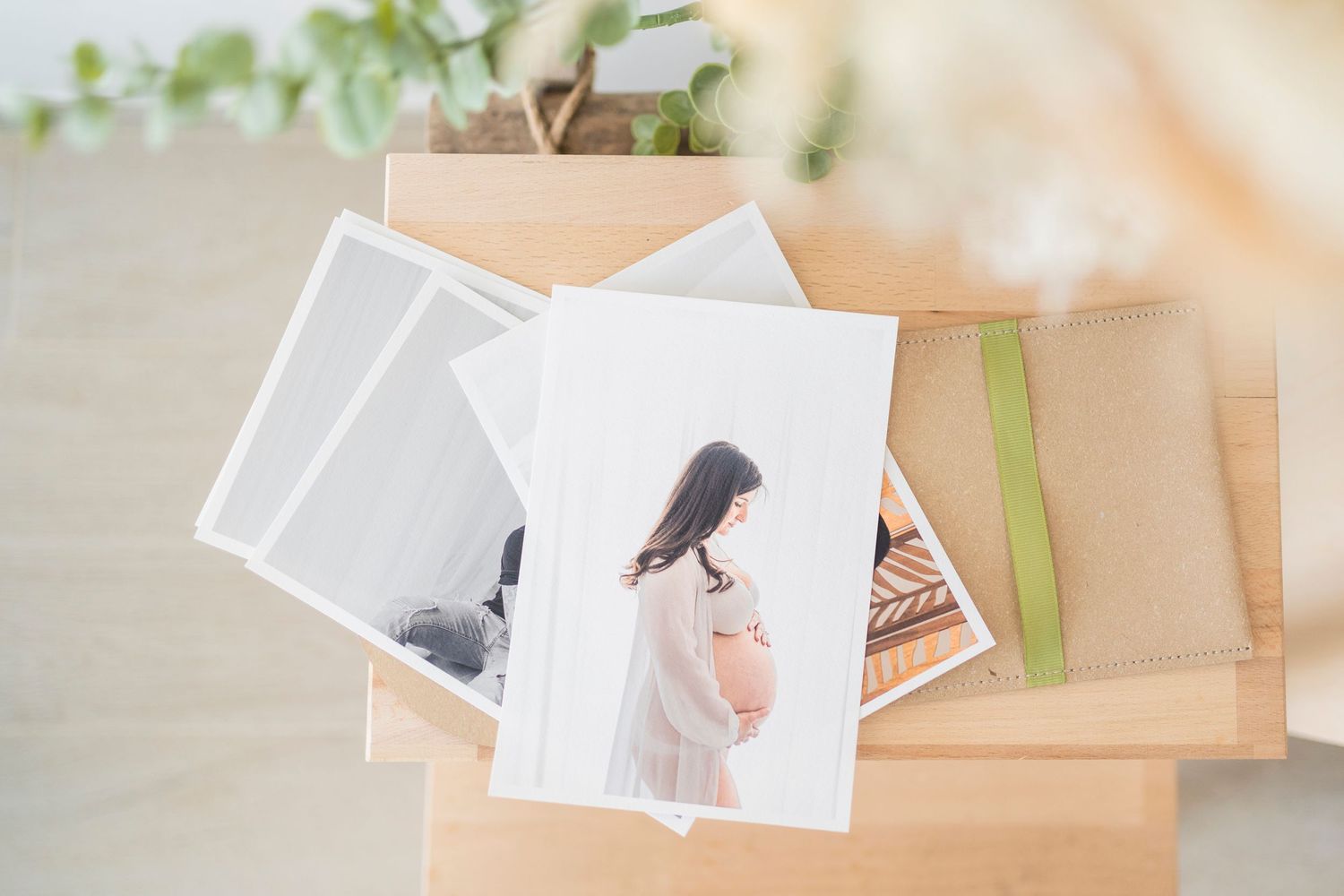Printed maternity photos in wooden box with ribbon on light wooden surface.